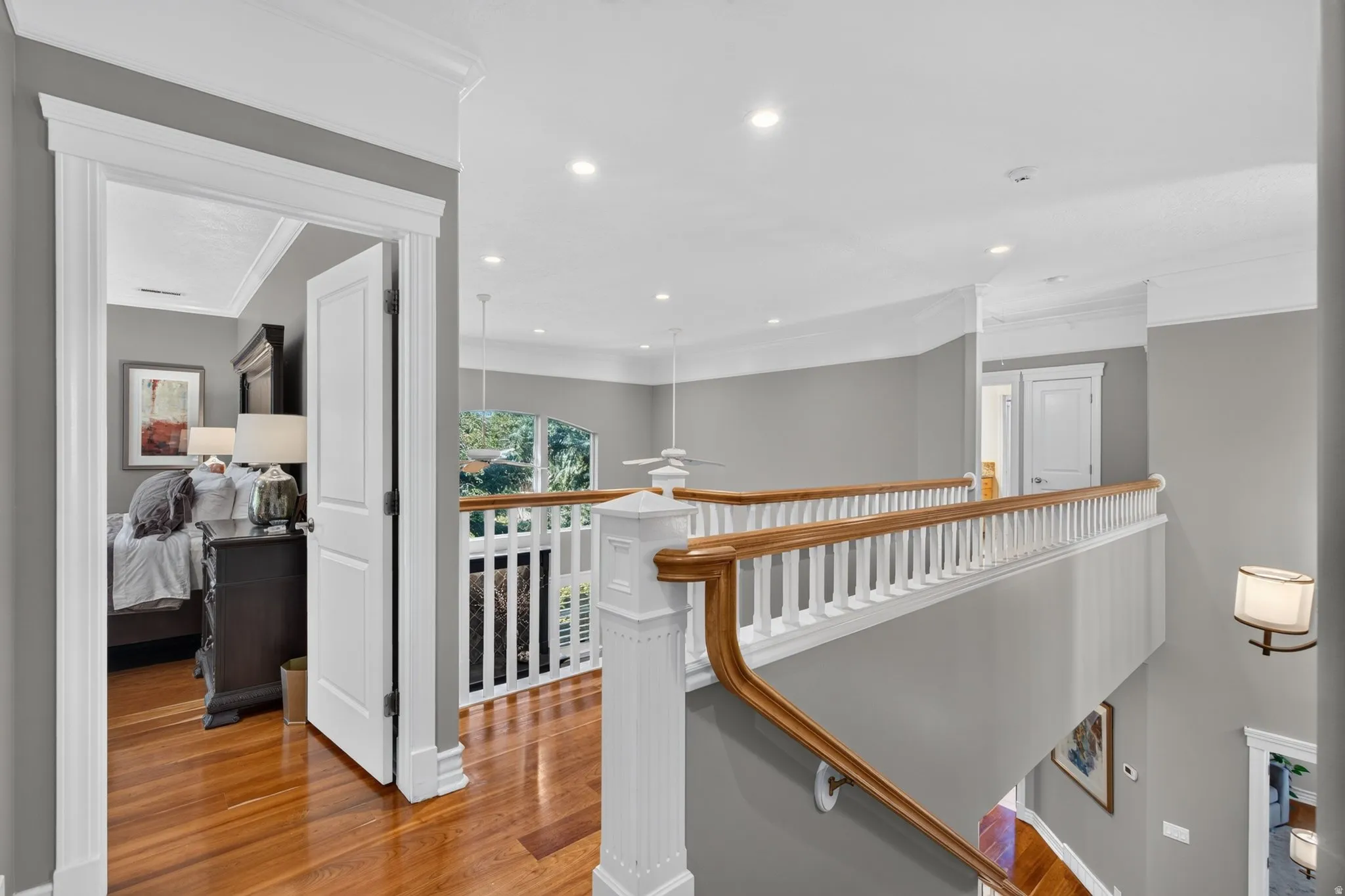 Hardwood flooring, white crown molding, recessed lighting, white paneled doors, and a wood and white banister