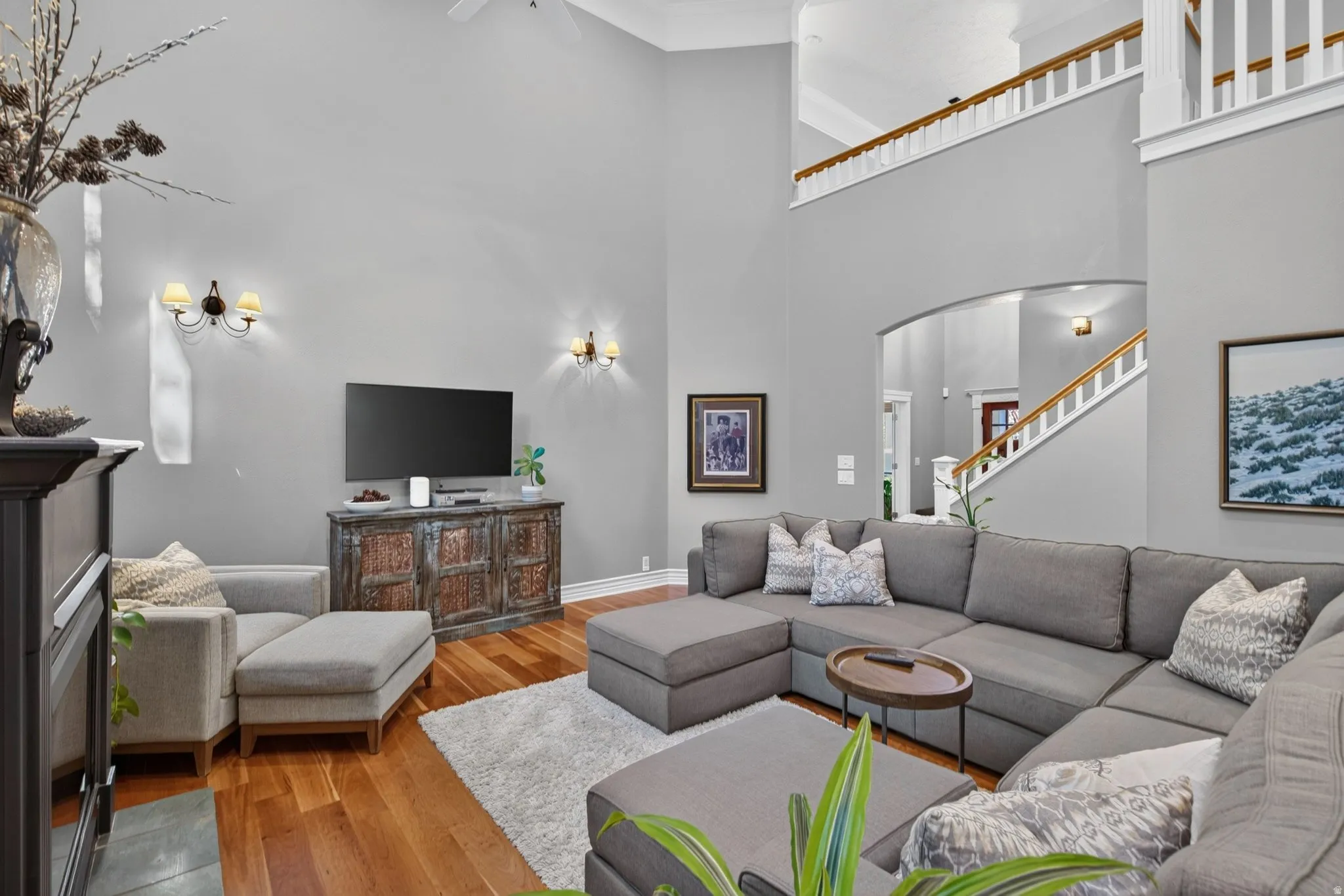 Two-story living area with high ceilings, wood-finish flooring, and sconce lighting