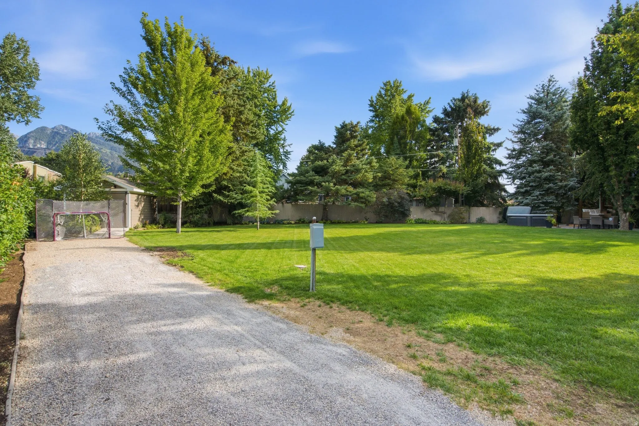 Expansive lawn bordered by mature trees and a gravel drive