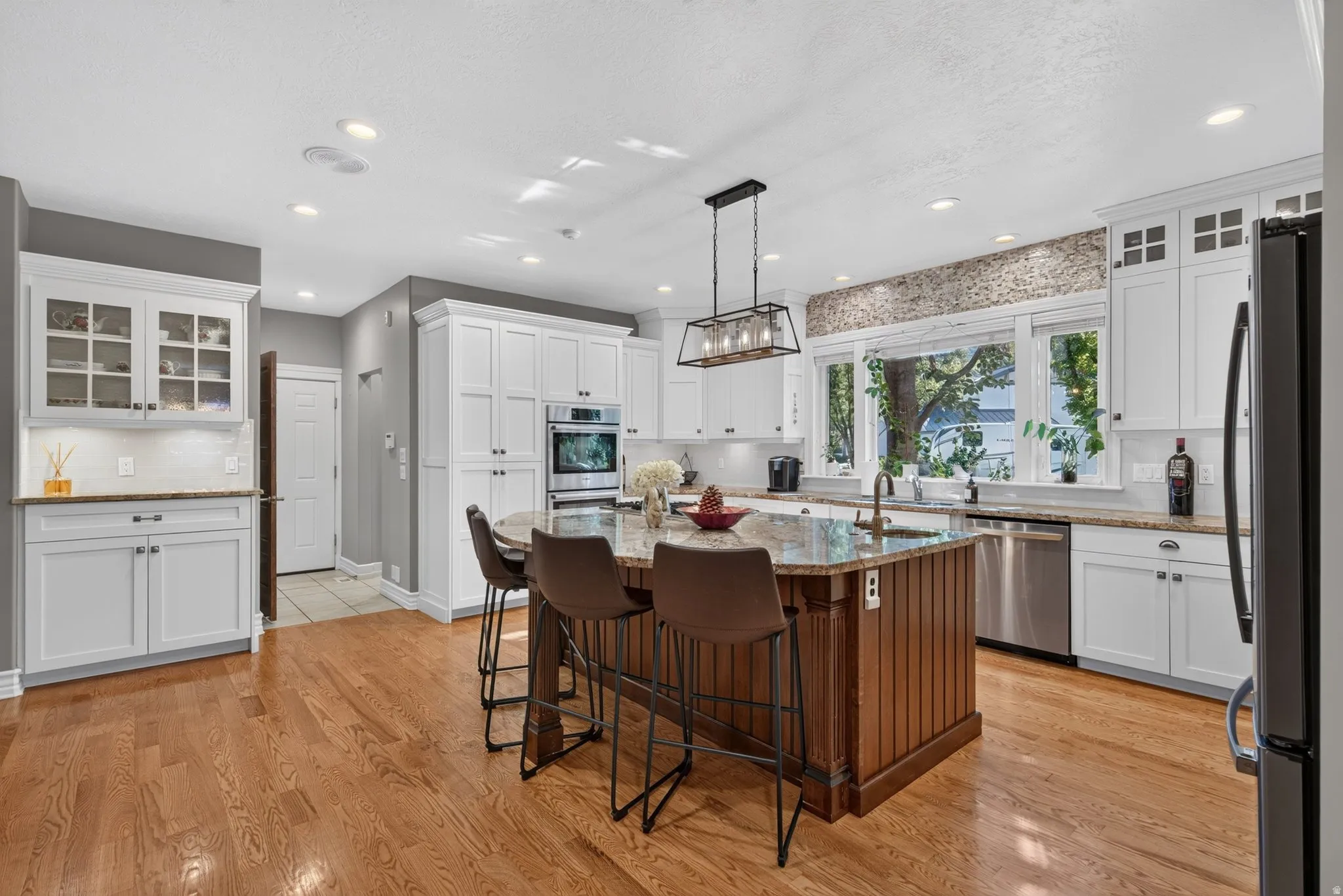 Spacious kitchen featuring an island with beadboard paneling, white cabinetry, integrated stainless steel appliances, wood-finish flooring, and a decorative tile backsplash