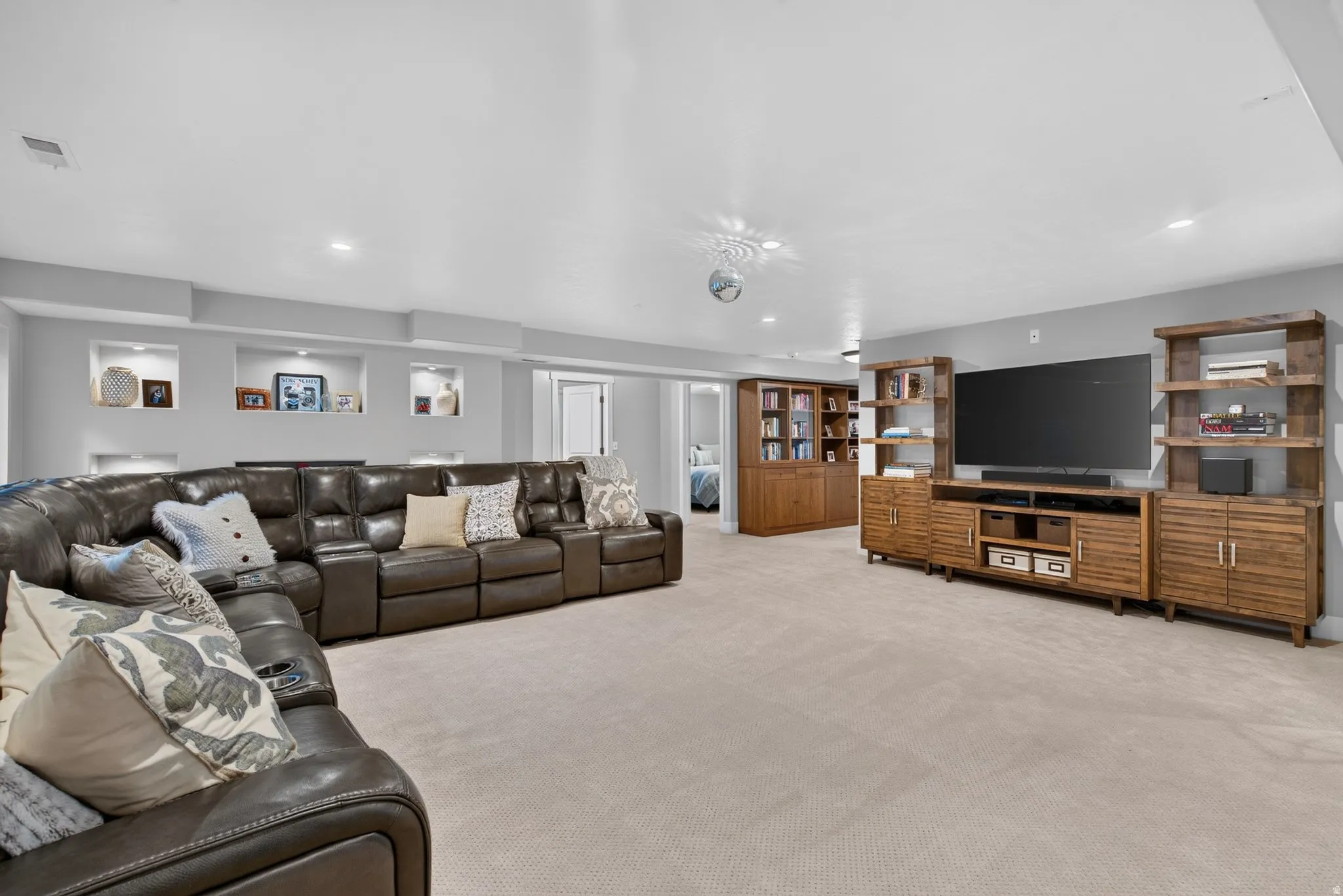 Recessed wall niches with integrated lighting, built-in media console with open shelving, and light-toned carpeting