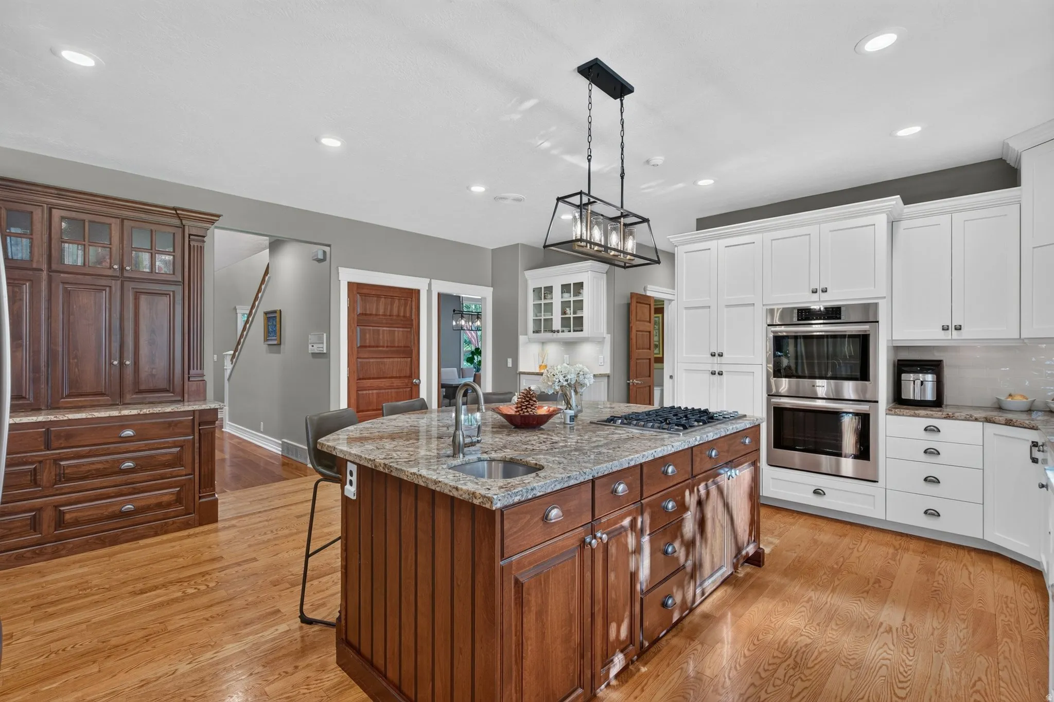 Spacious kitchen featuring an expansive center island with a built-in cooktop, light wood-finish flooring, white perimeter cabinetry, and integrated stainless steel double ovens