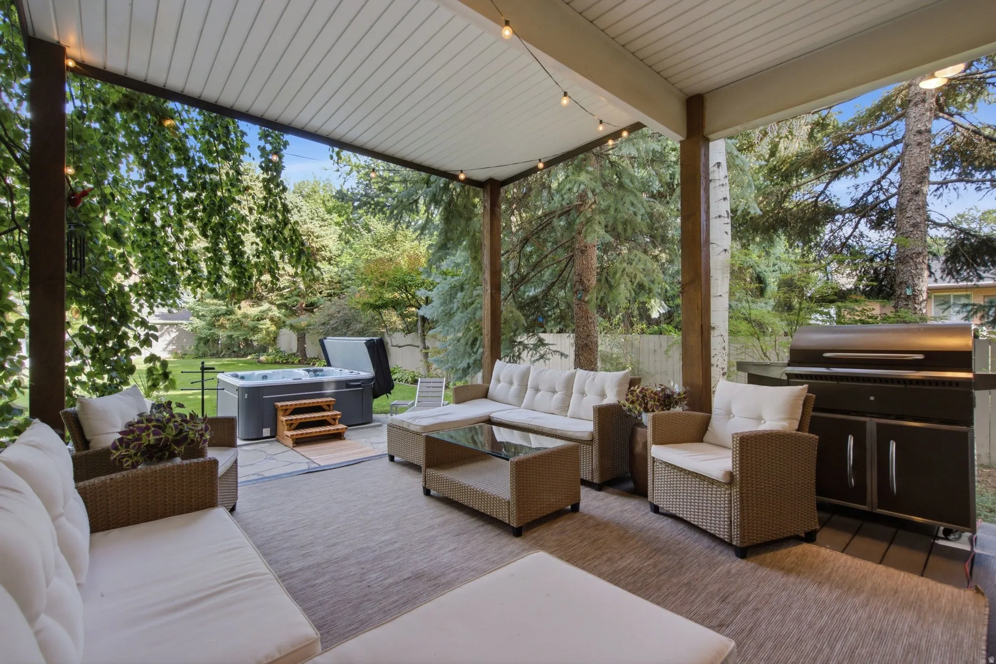 Covered patio with string lighting, a built-in grill, a hot tub, and a spacious outdoor rug