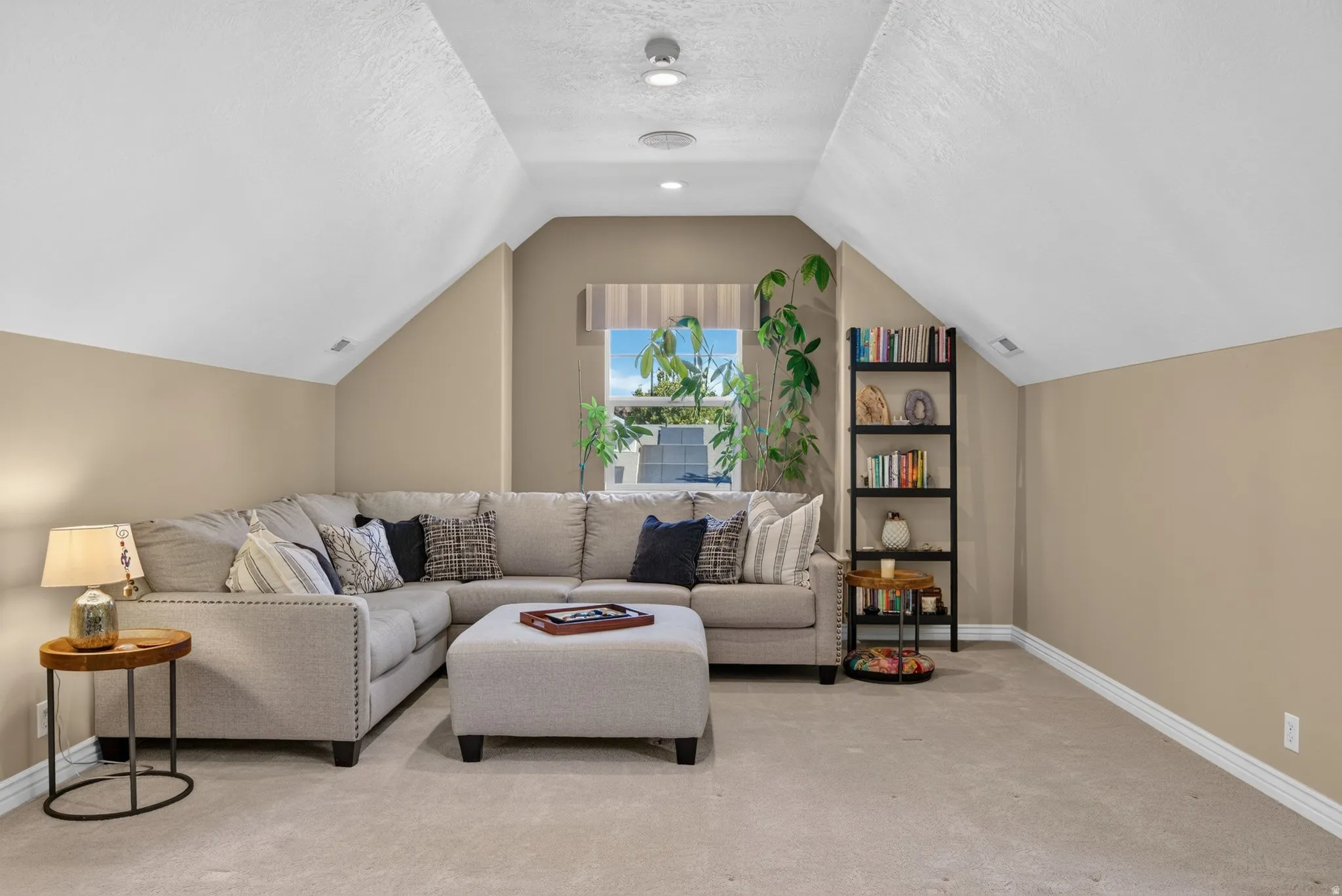 Recessed lighting illuminates a spacious room featuring sloped ceilings and neutral-toned carpeting