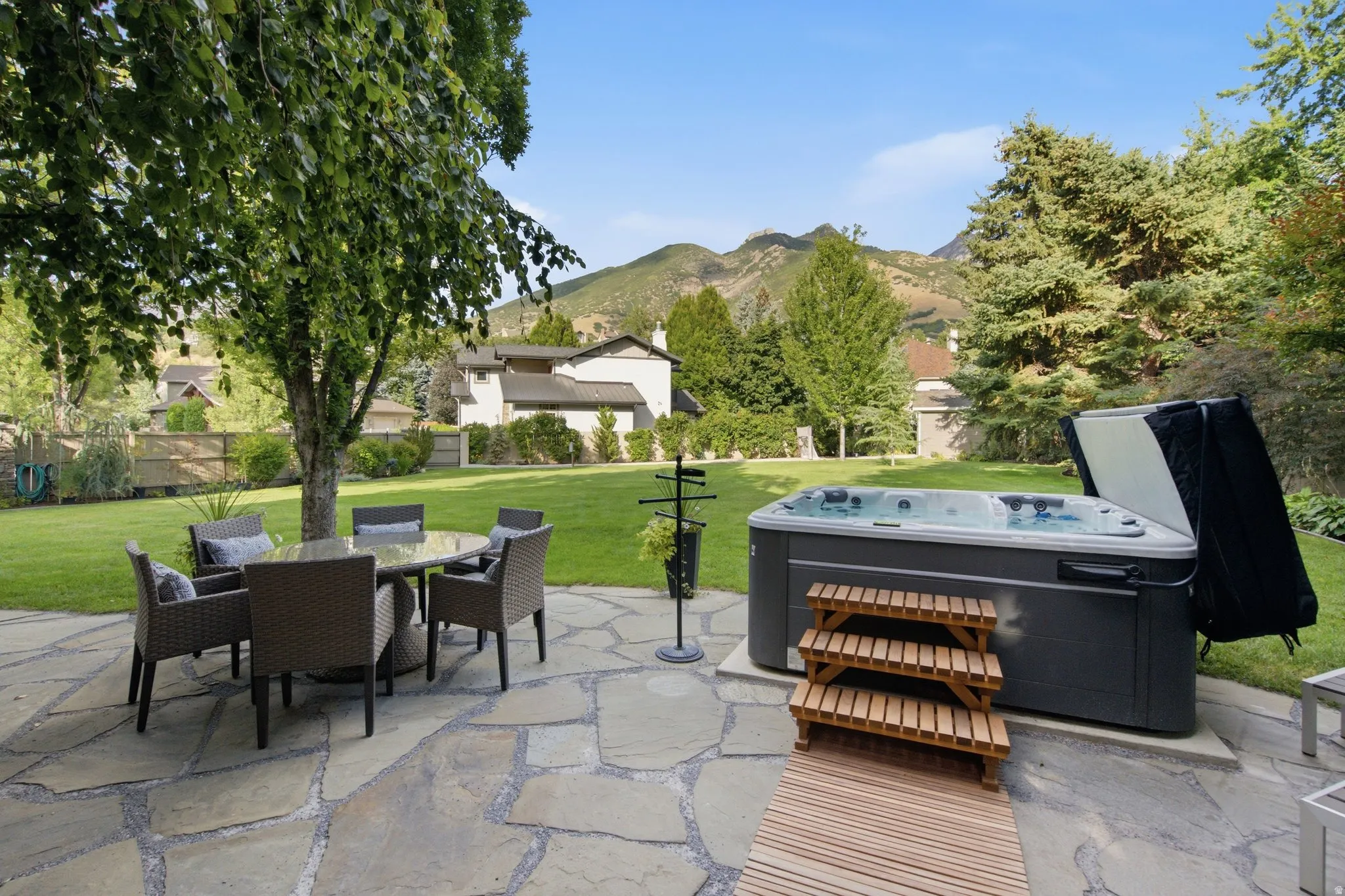 Expansive backyard featuring a natural stone patio, mature trees, a manicured lawn, and a built-in hot tub