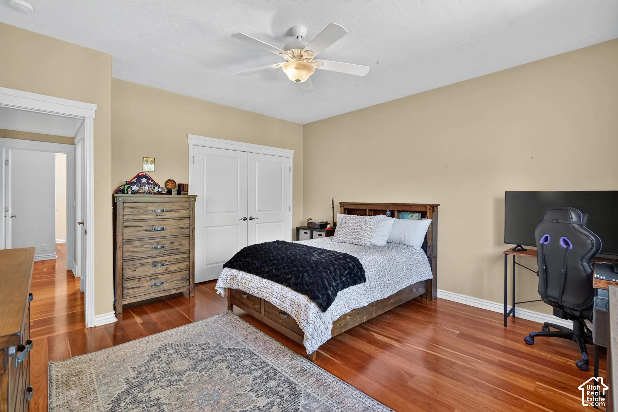 Warm-toned wood-finish flooring, a ceiling fan with integrated lighting, and white bi-fold closet doors