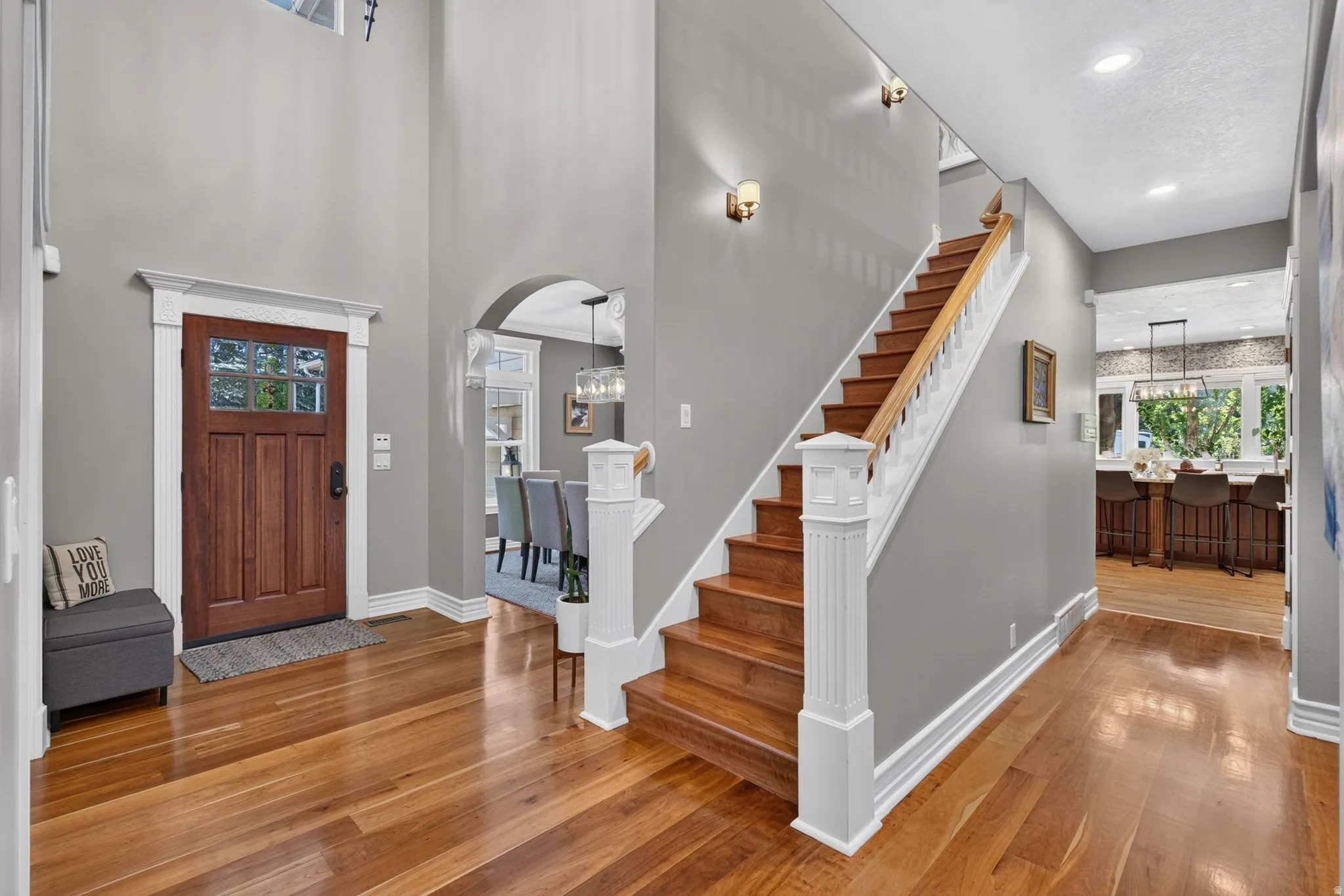 Hardwood flooring throughout the entry, a wood-paneled door with glass inserts, a two-story foyer with sconce lighting, an arched doorway, and a wood staircase with white balusters