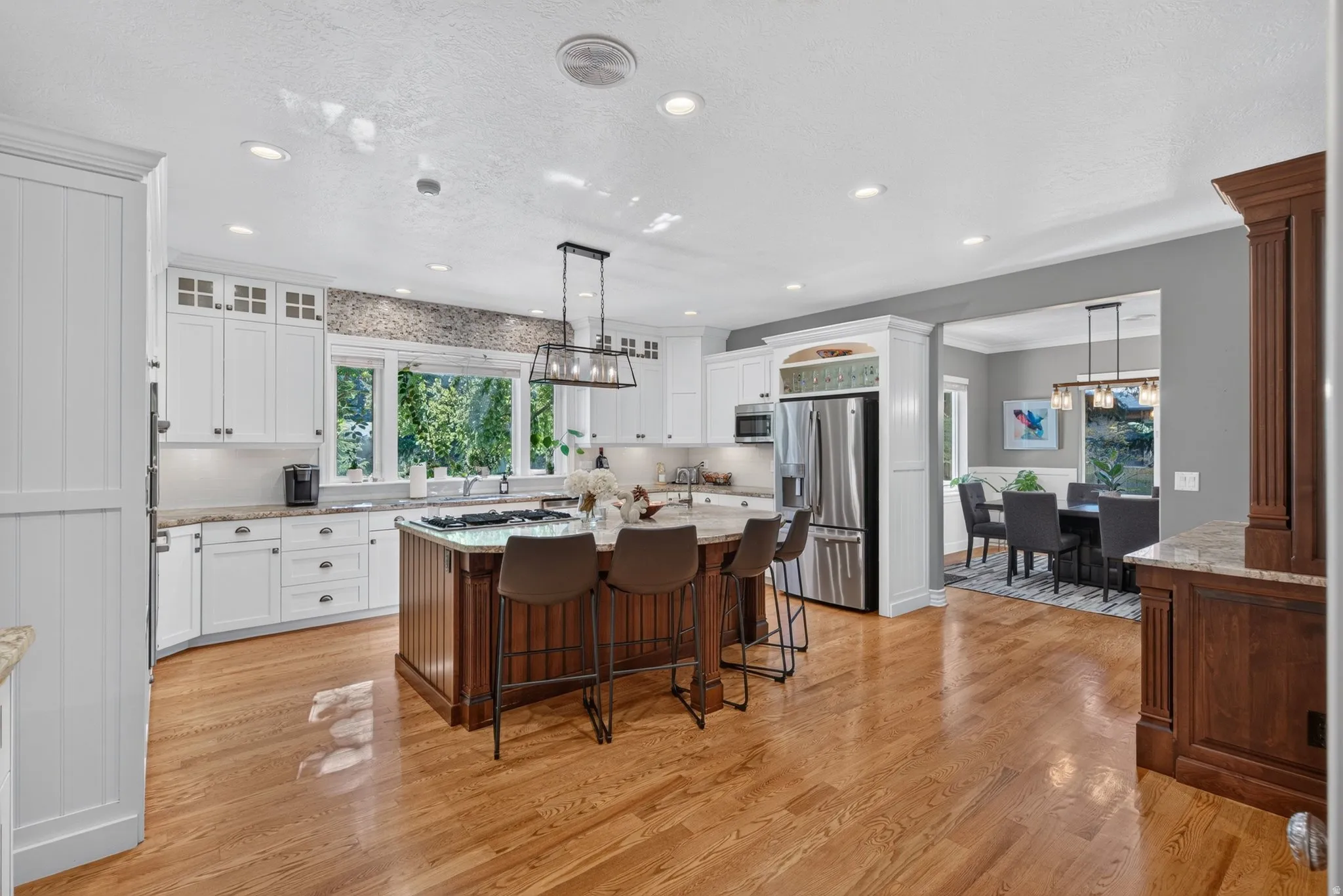 Kitchen featuring hardwood flooring, white cabinetry, a built-in stainless steel refrigerator, a center island with seating, and recessed lighting