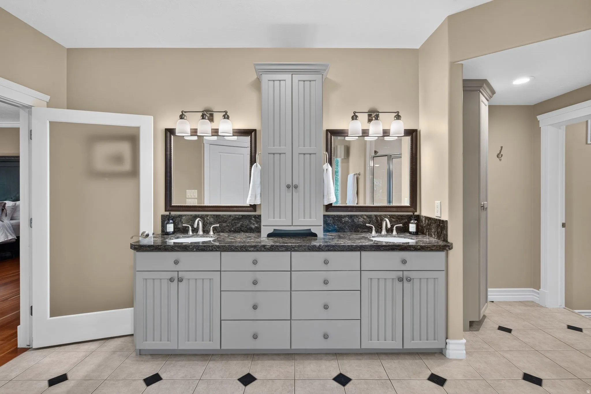 Dual vanities with undermount sinks, stone countertops, gray shaker-style cabinetry, and a central built-in storage tower