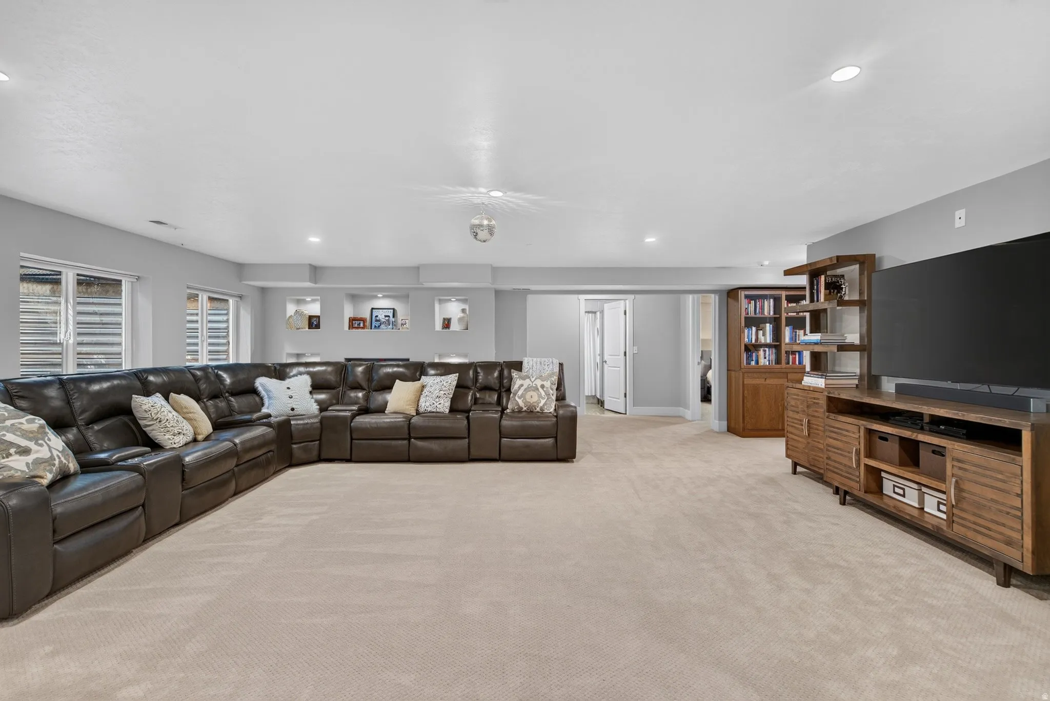 Recessed lighting, built-in shelving, and neutral wall tones enhance this expansive carpeted space