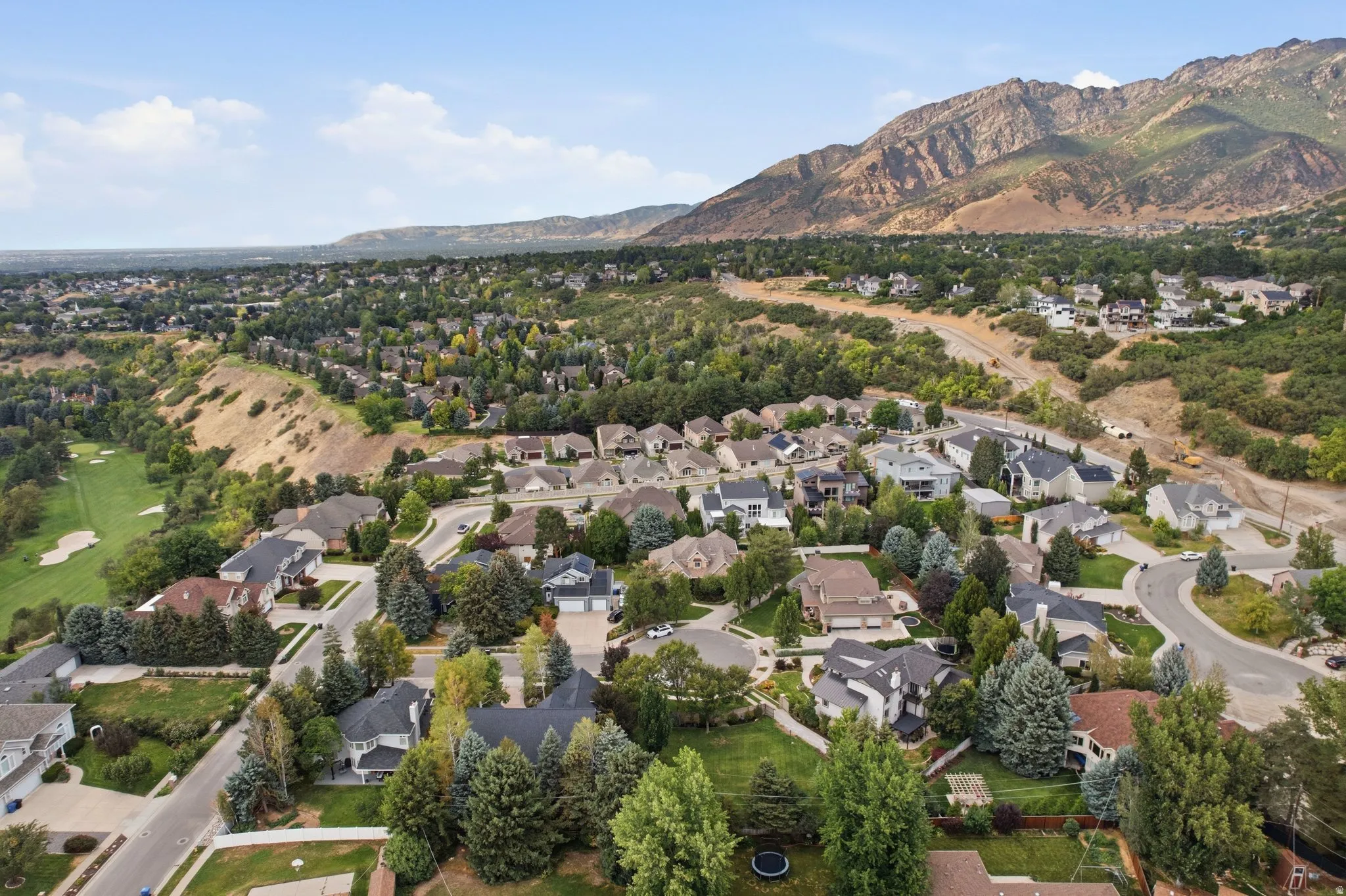 Expansive residential area with mature tree landscaping, mountainous backdrop, and golf course access