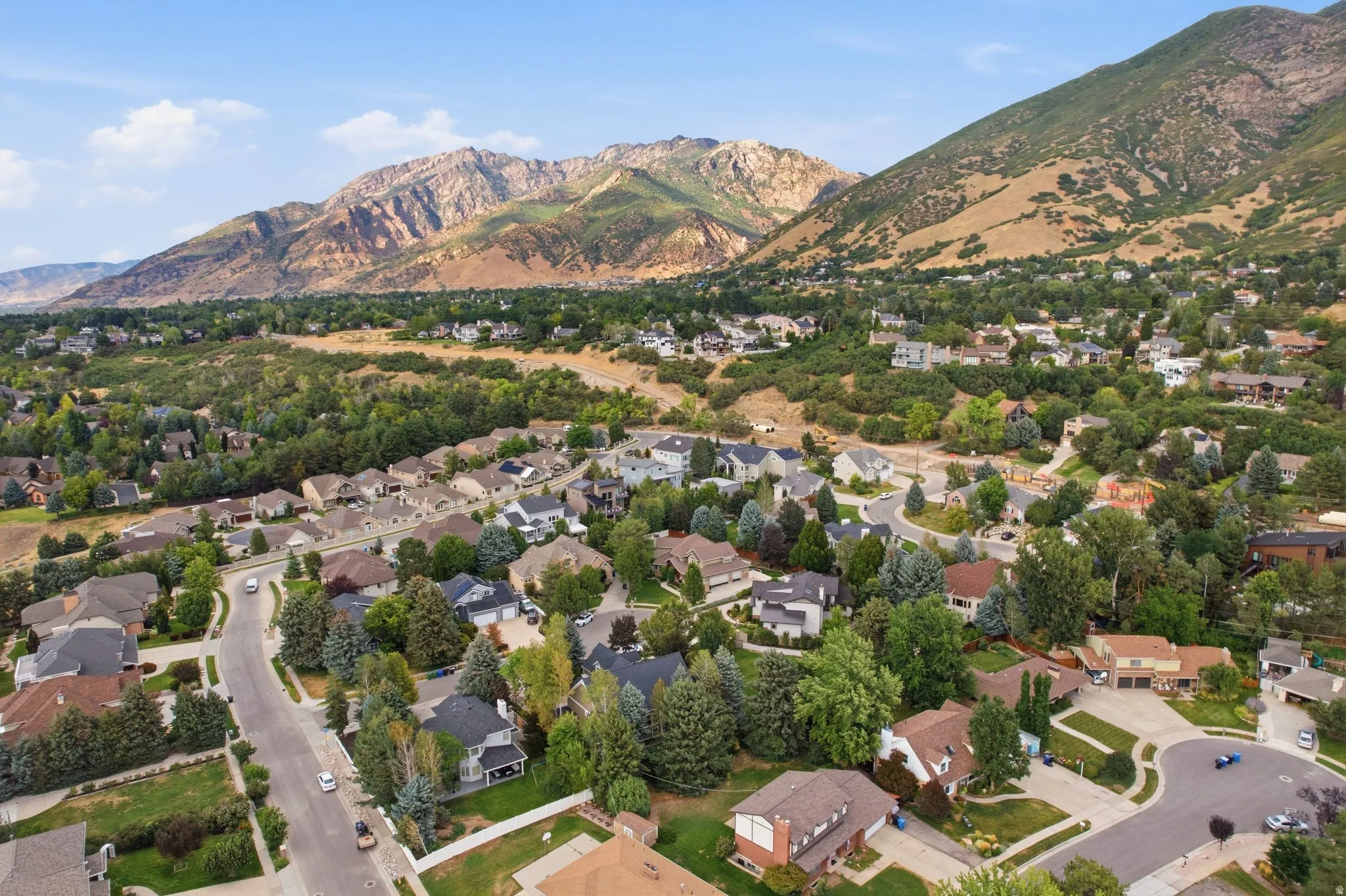 Residential neighborhood with established homes, mature trees, paved streets, and mountainous surroundings
