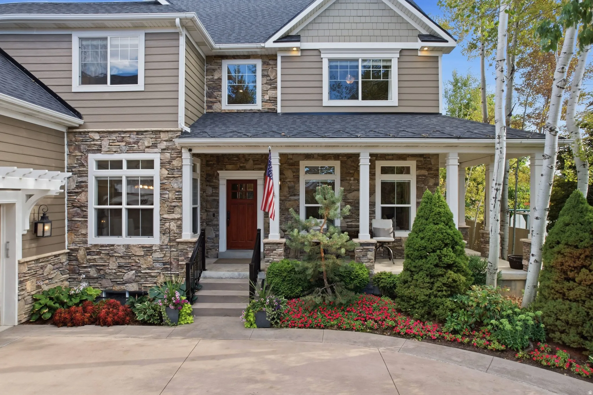 Stone and siding exterior with a covered porch, wood entry door, and manicured landscaping