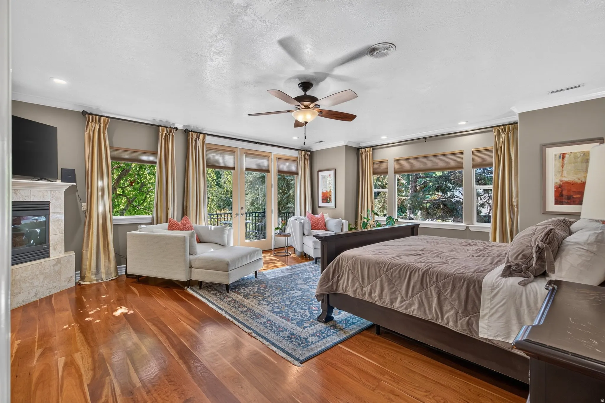 Hardwood flooring, recessed lighting, ceiling fan, fireplace with stone surround, and French doors