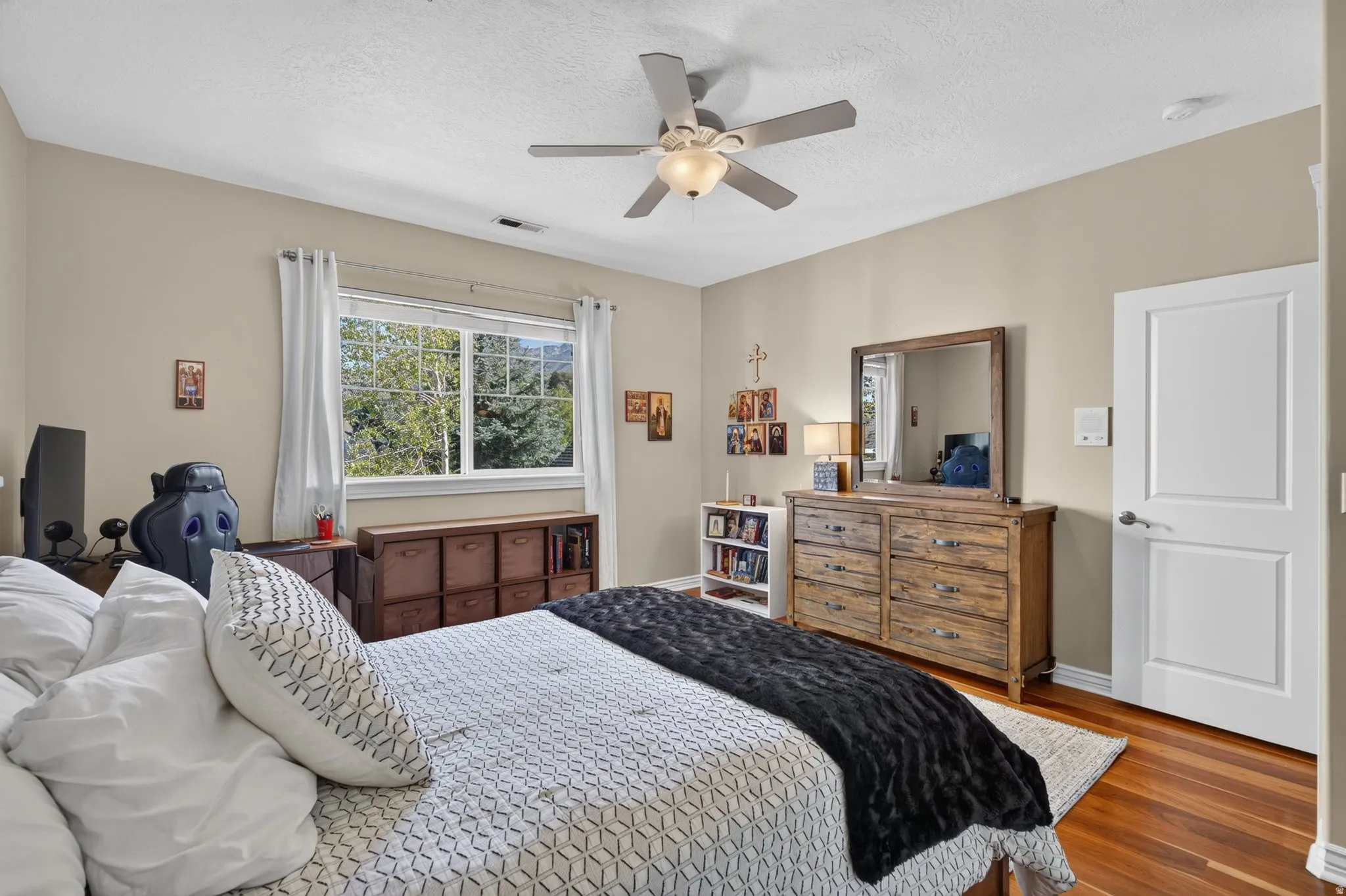 Wood-finish flooring, ceiling fan with integrated lighting, natural light window, neutral wall paint, and a two-panel interior door