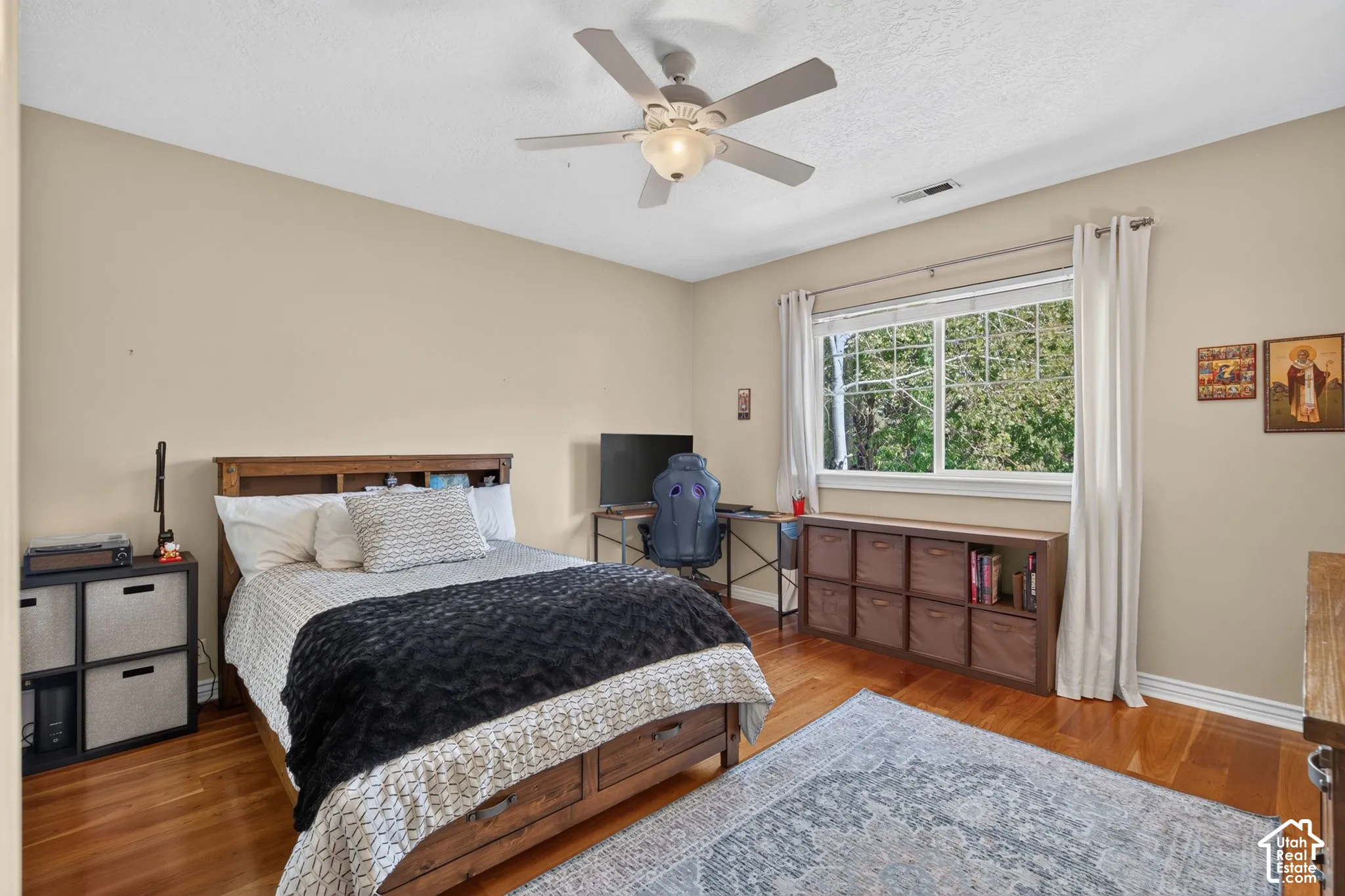 Wood-finish flooring, overhead ceiling fan, window with white trim, and neutral wall tones