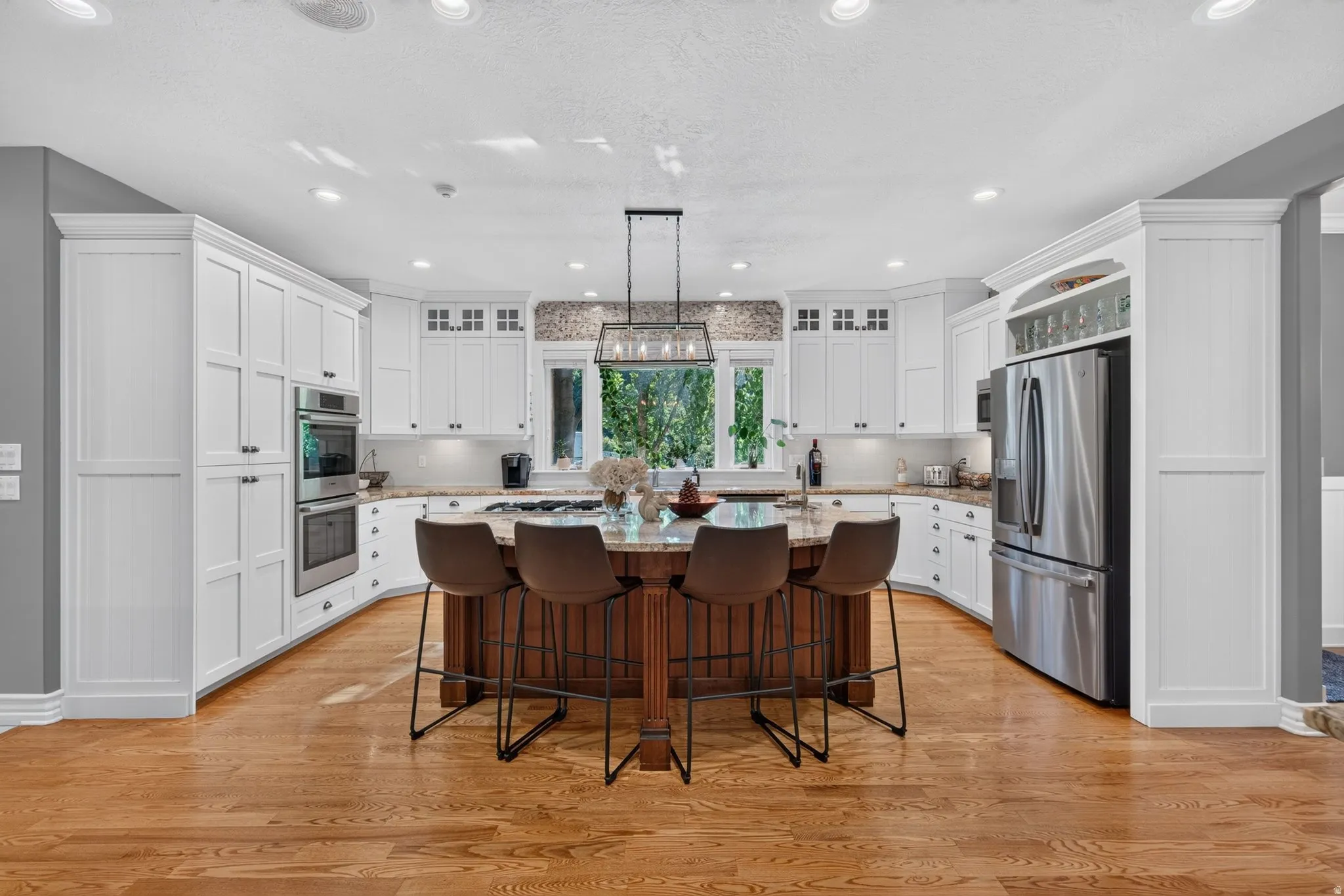 Spacious kitchen featuring white cabinetry, a large central island with seating, stainless steel appliances, wood-finish flooring, and recessed lighting