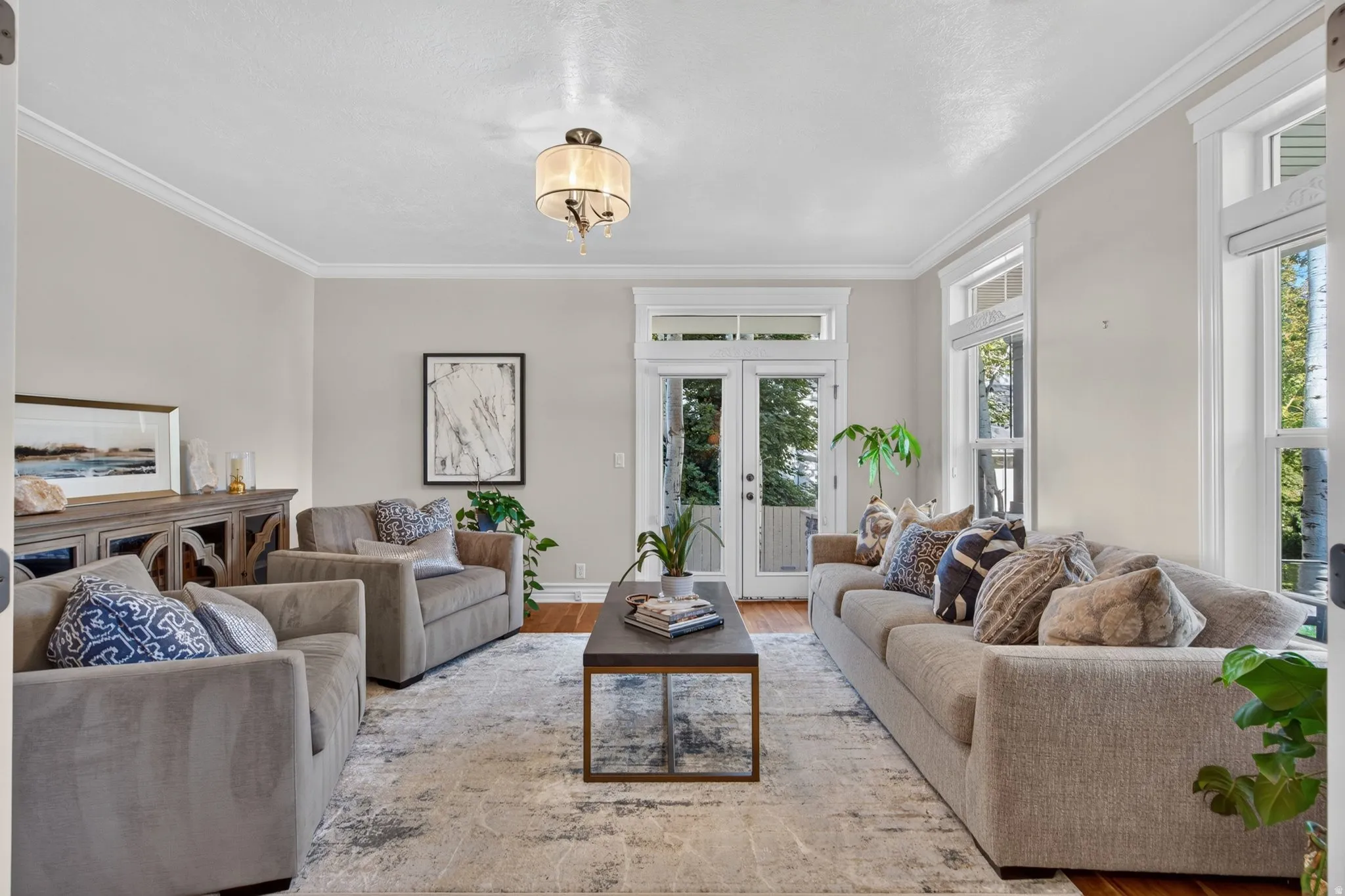 Hardwood flooring, crown molding, double French doors, large windows, and a chandelier with a drum shade