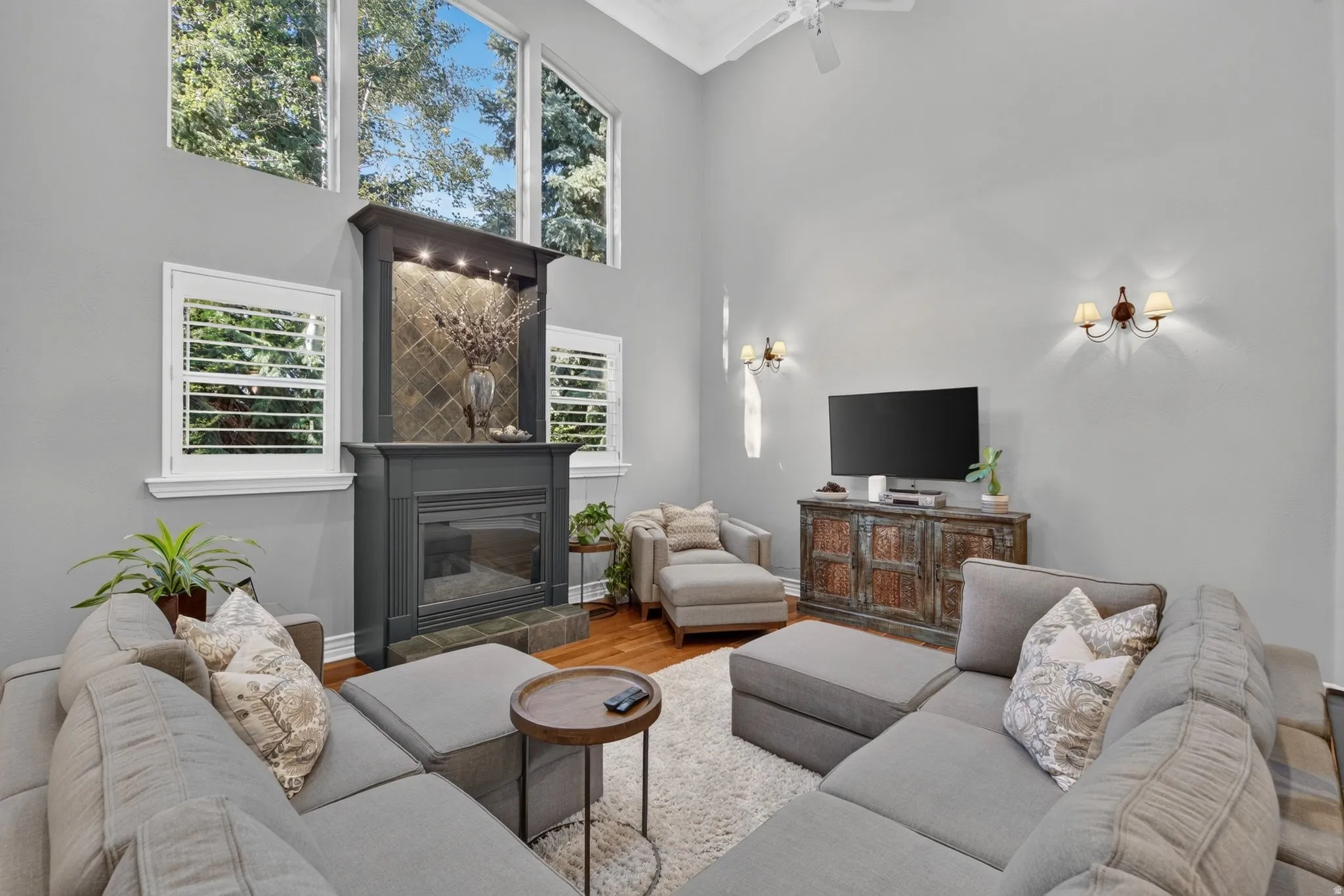 Vaulted ceiling with a ceiling fan, fireplace with a tile surround and mantel, plantation shutters, and hardwood flooring