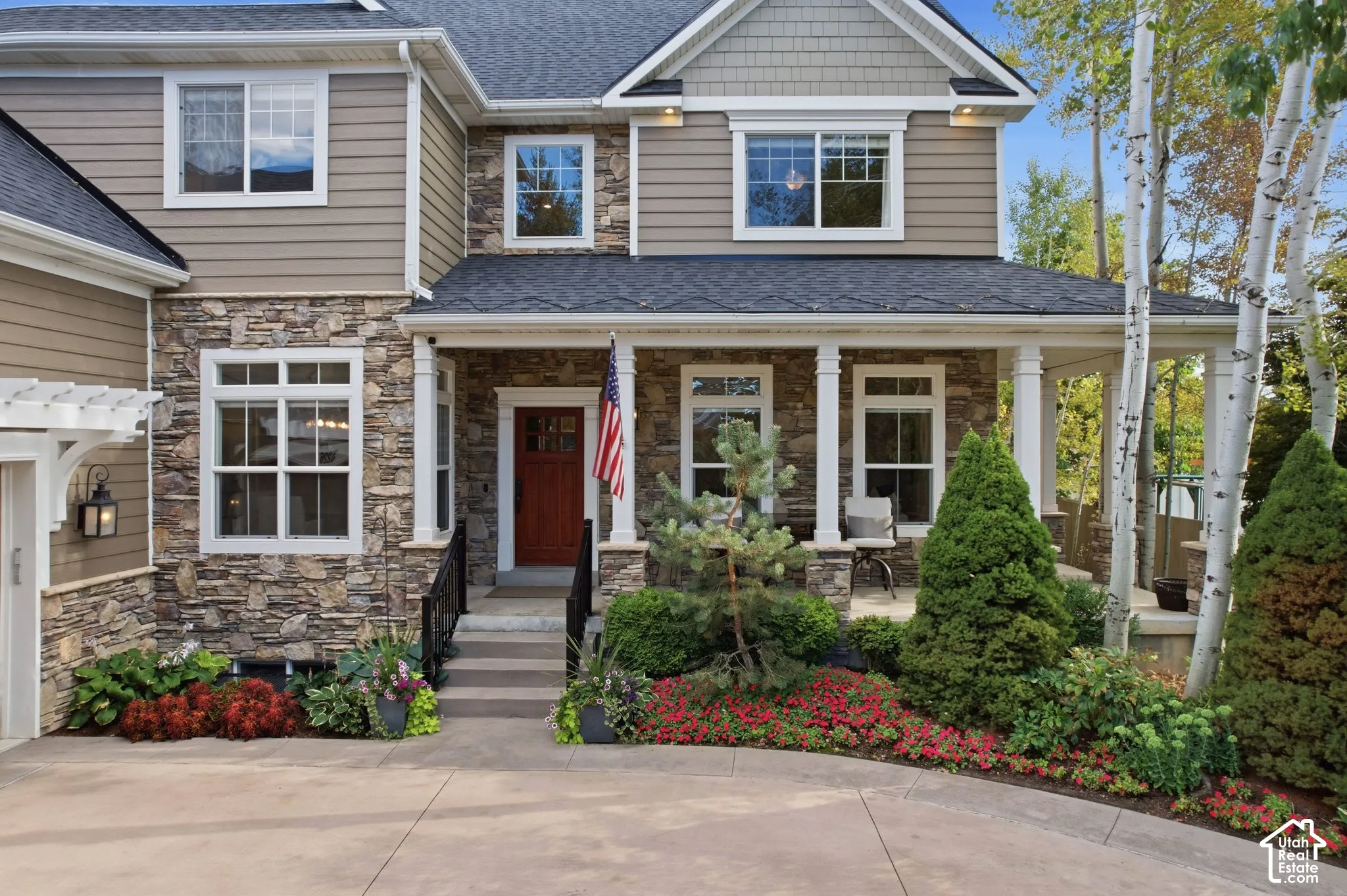Stone and siding exterior with a covered porch, wood entry door, and manicured landscaping