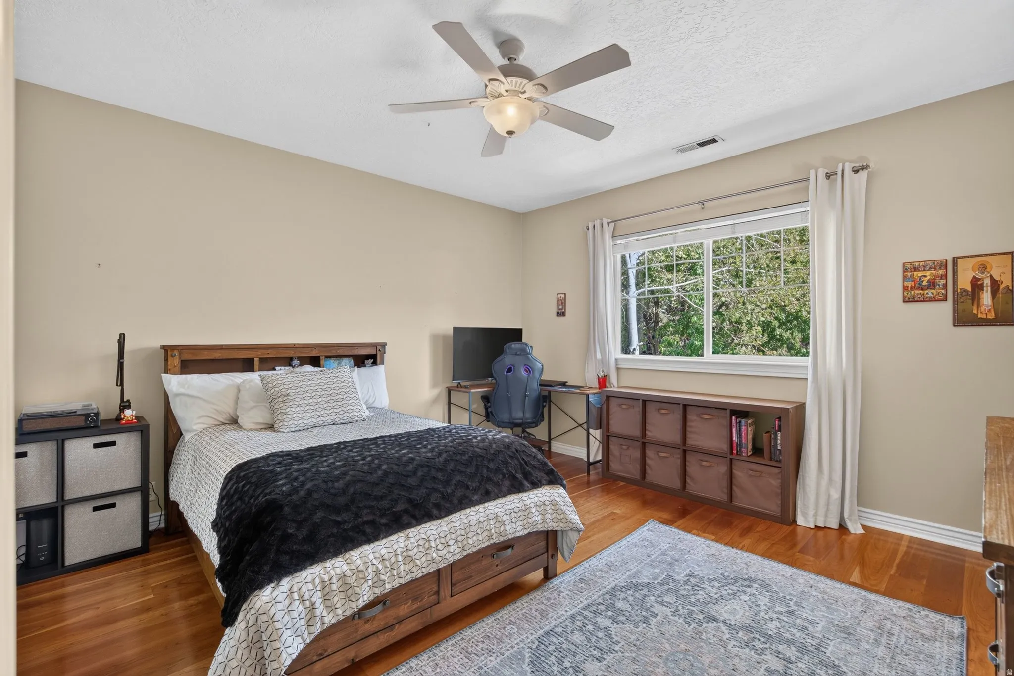 Wood-finish flooring, overhead ceiling fan, window with white trim, and neutral wall tones