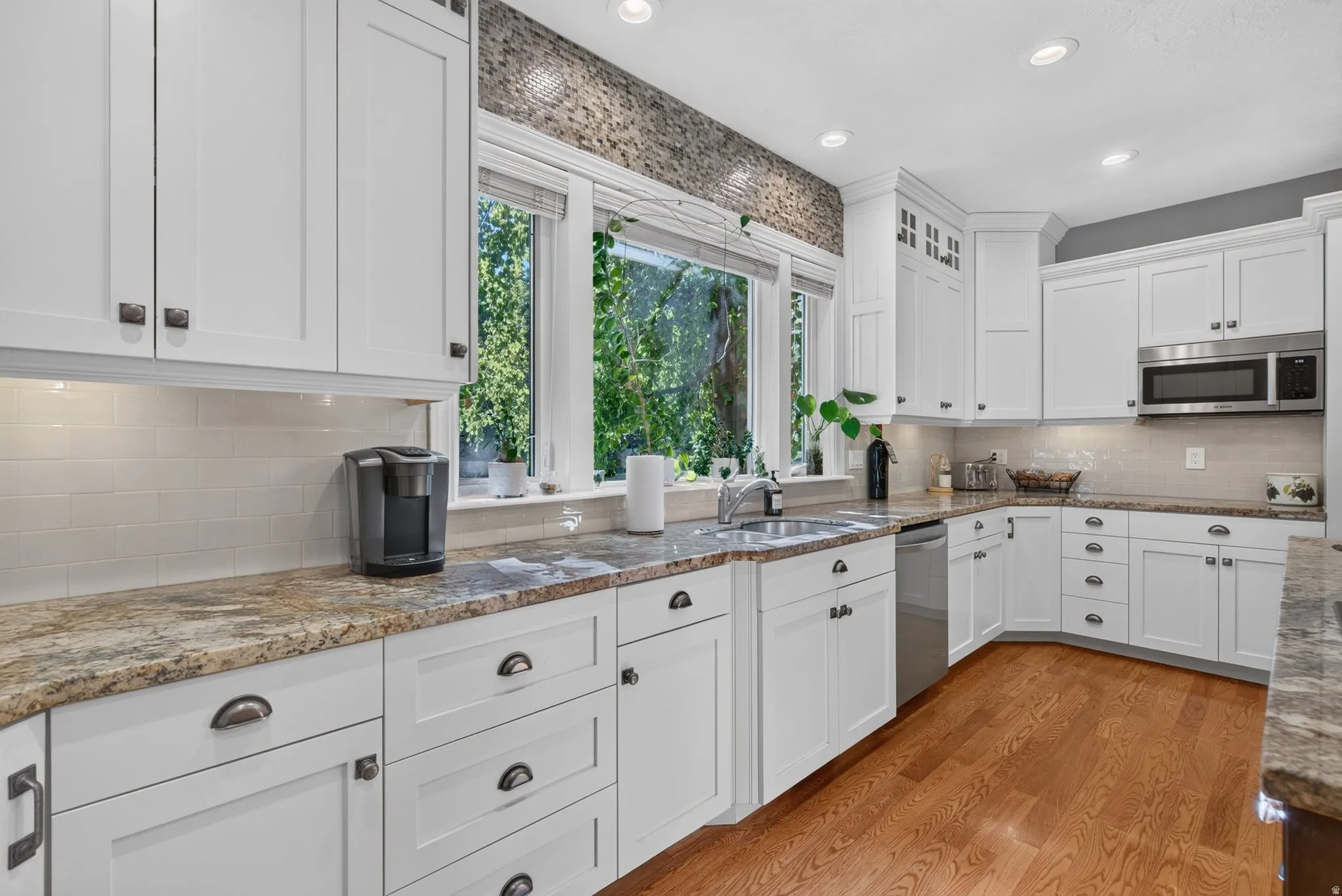 Updated kitchen featuring white cabinetry, stone countertops, stainless steel appliances, a tile backsplash, and wood-finish flooring