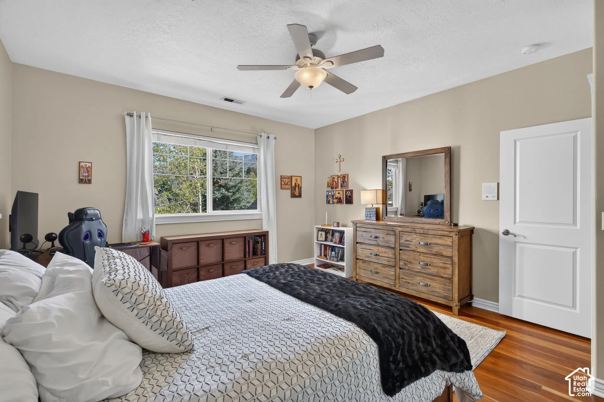 Wood-finish flooring, ceiling fan with integrated lighting, natural light window, neutral wall paint, and a two-panel interior door