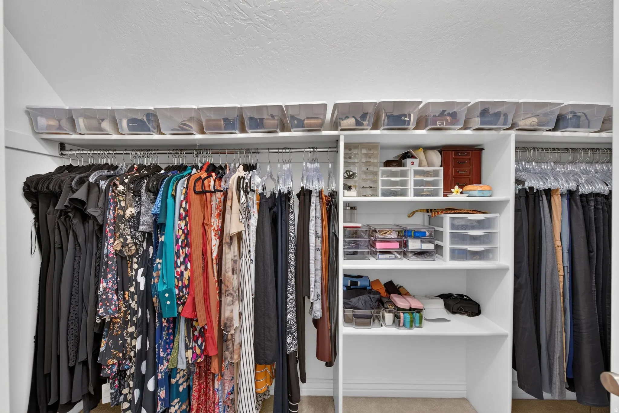 Built-in closet system featuring multiple hanging rods, white shelving, and overhead storage