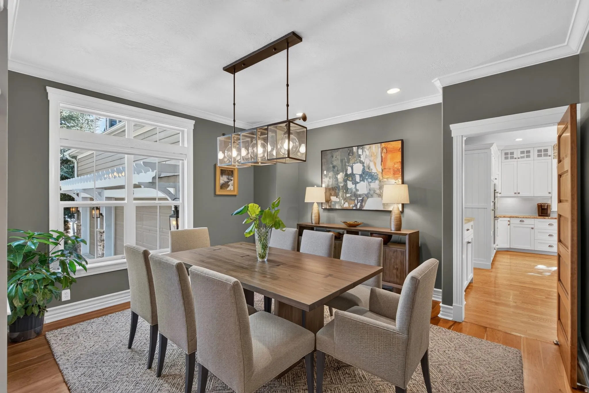 Dining area featuring wood-finish flooring, a large window with transom, crown molding, and a multi-light linear chandelier