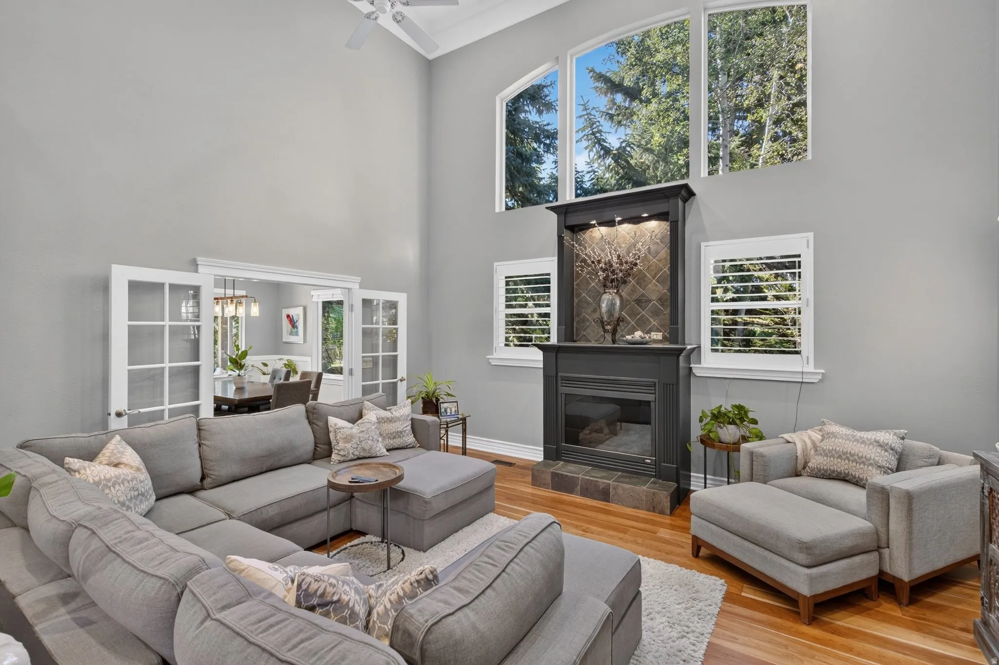 Two-story ceiling, hardwood flooring, fireplace with a tiled surround, arched windows, and French doors