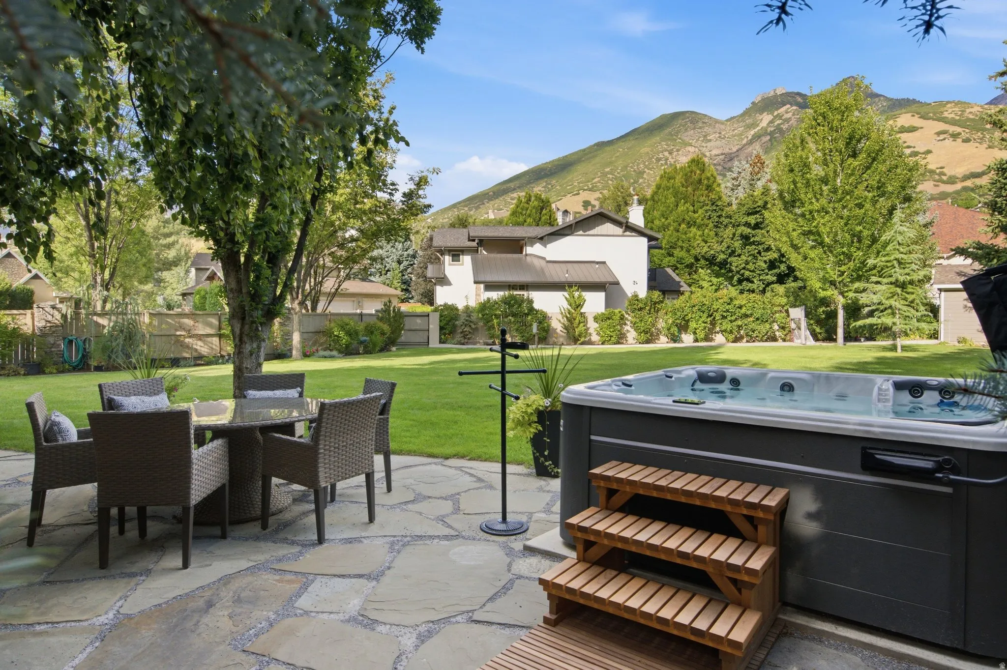 Expansive backyard featuring a natural stone patio, integrated hot tub with wood steps, and a large grassy area