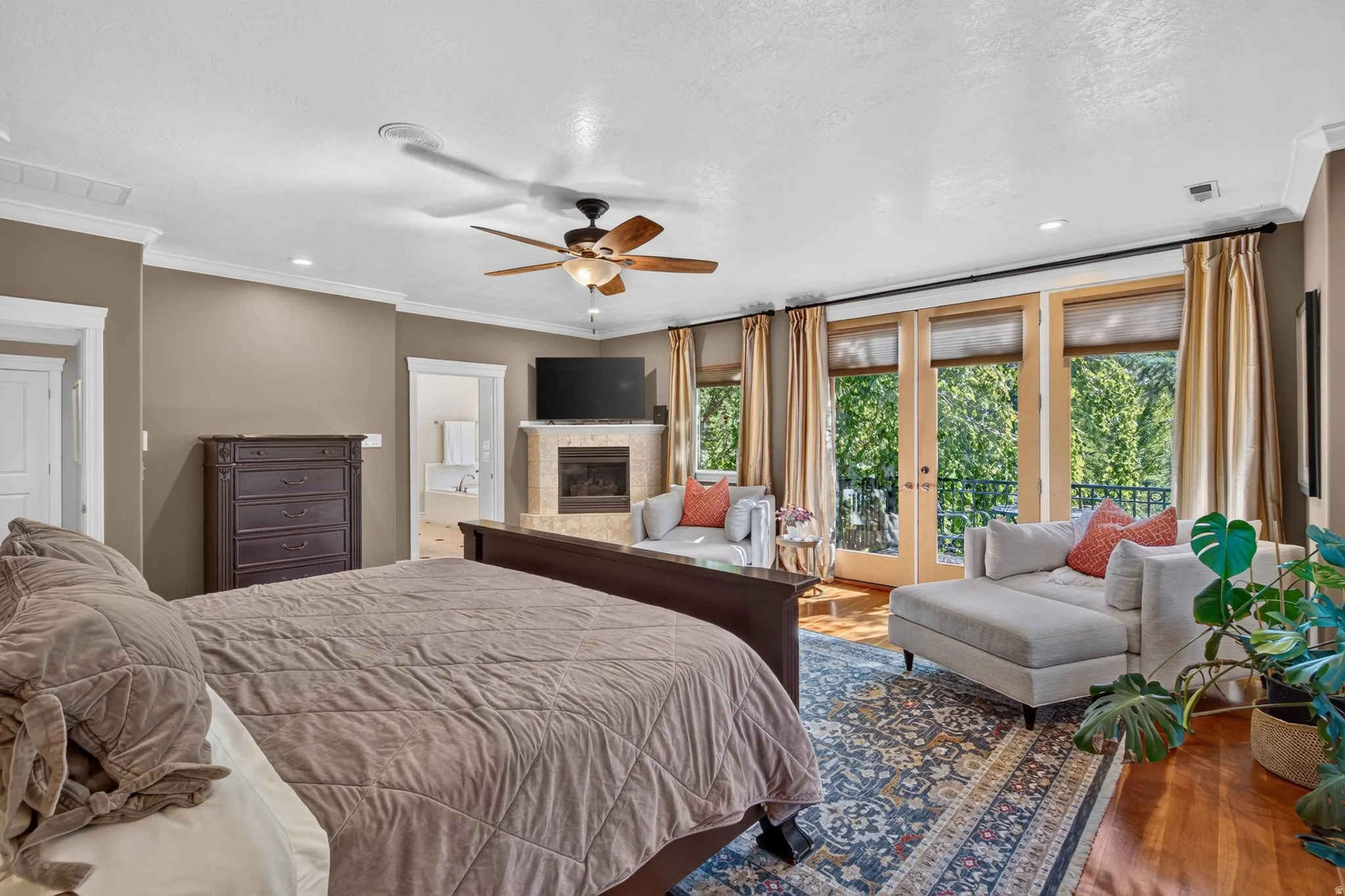Hardwood flooring, ceiling fan, crown molding, double French doors with transom windows, and a built-in fireplace with stone surround