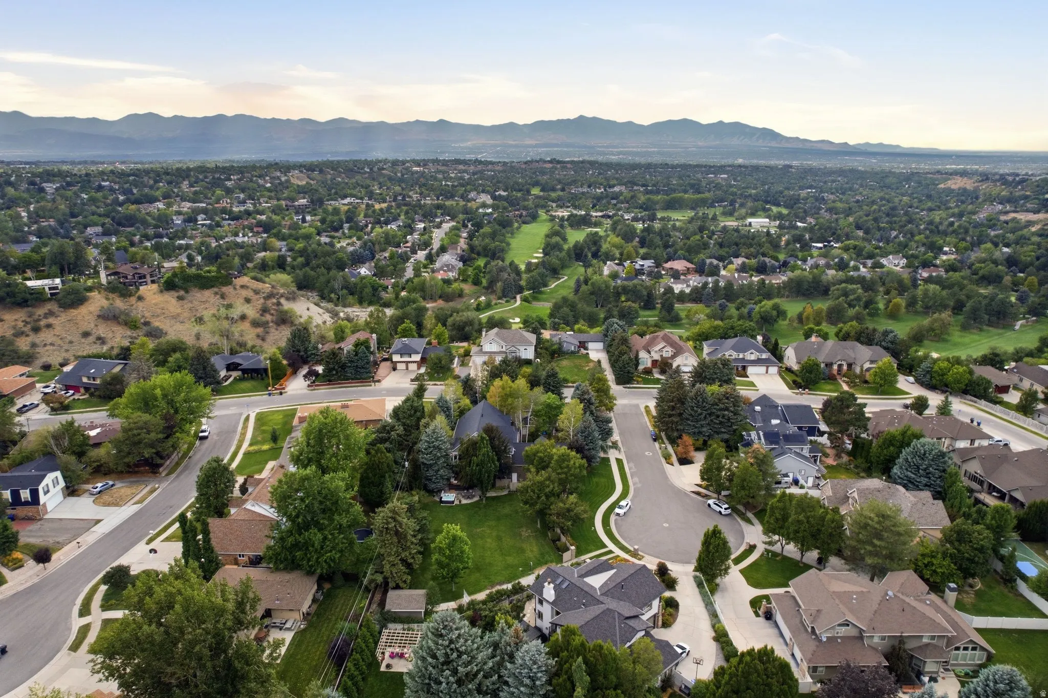Expansive residential area with mature tree coverage, mountain backdrop, and golf course terrain