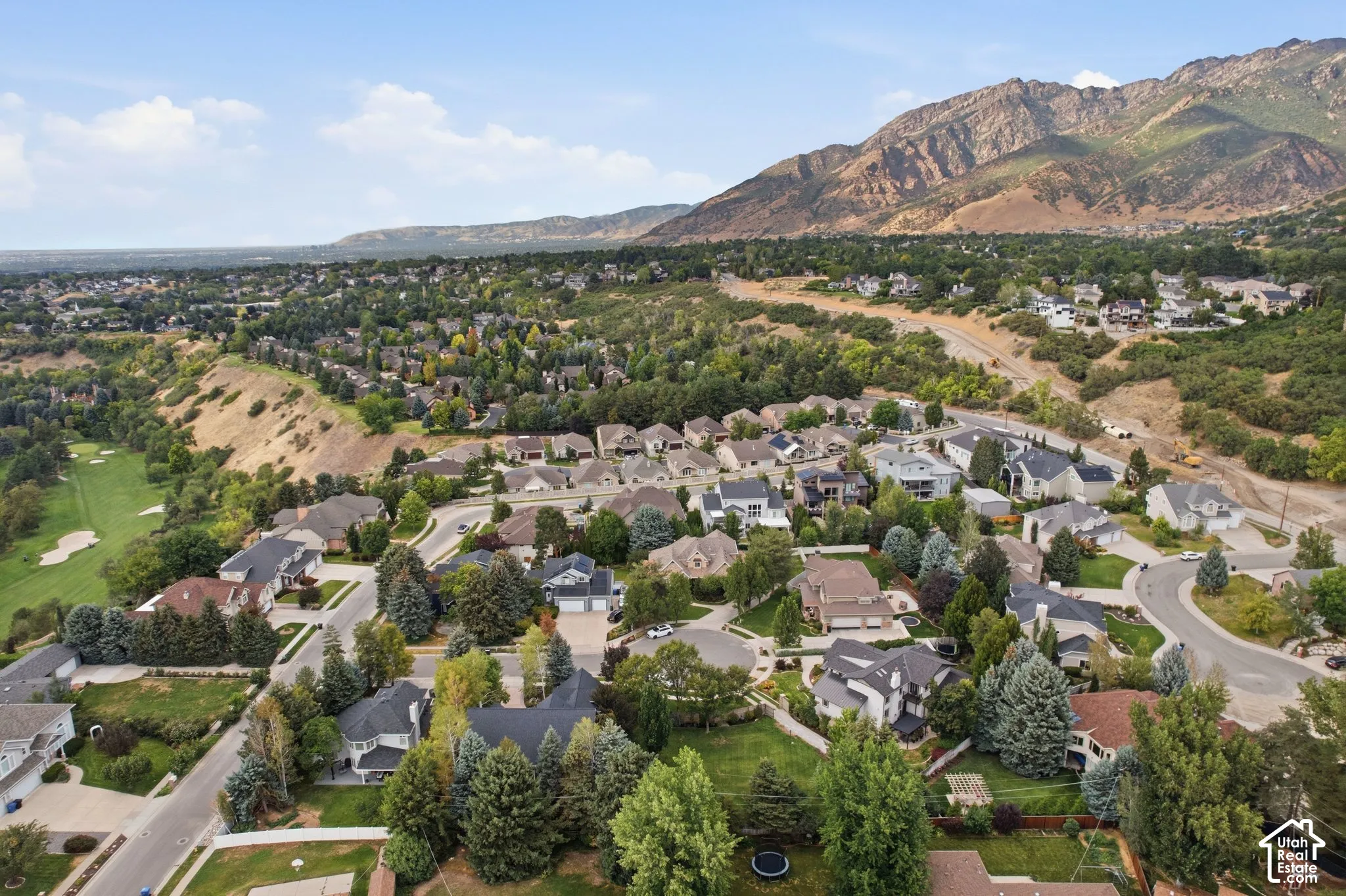 Expansive residential area with mature tree landscaping, mountainous backdrop, and golf course access