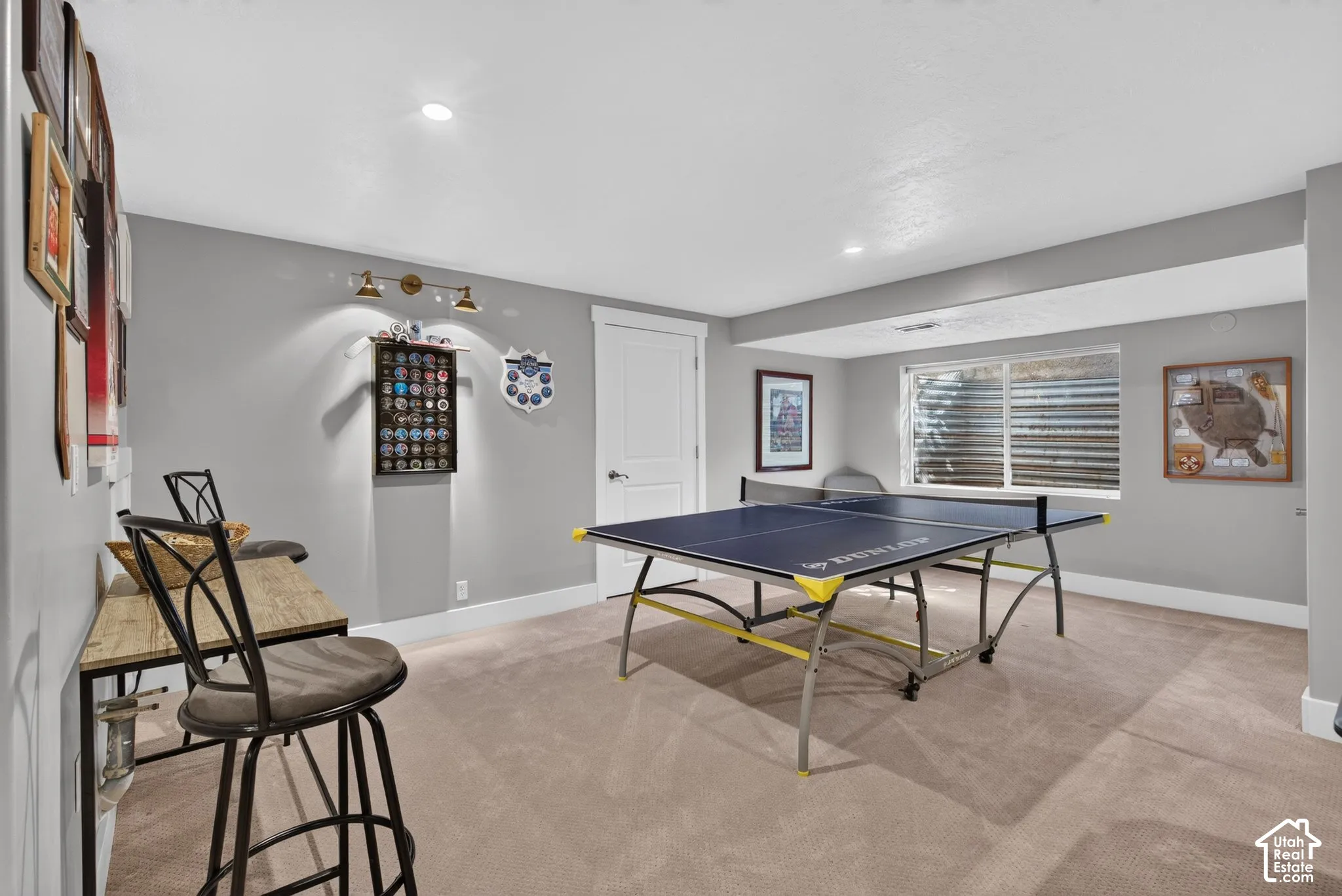 Recessed lighting, wall-mounted fixtures, window with blinds, light gray wall paint, and light-colored carpeting