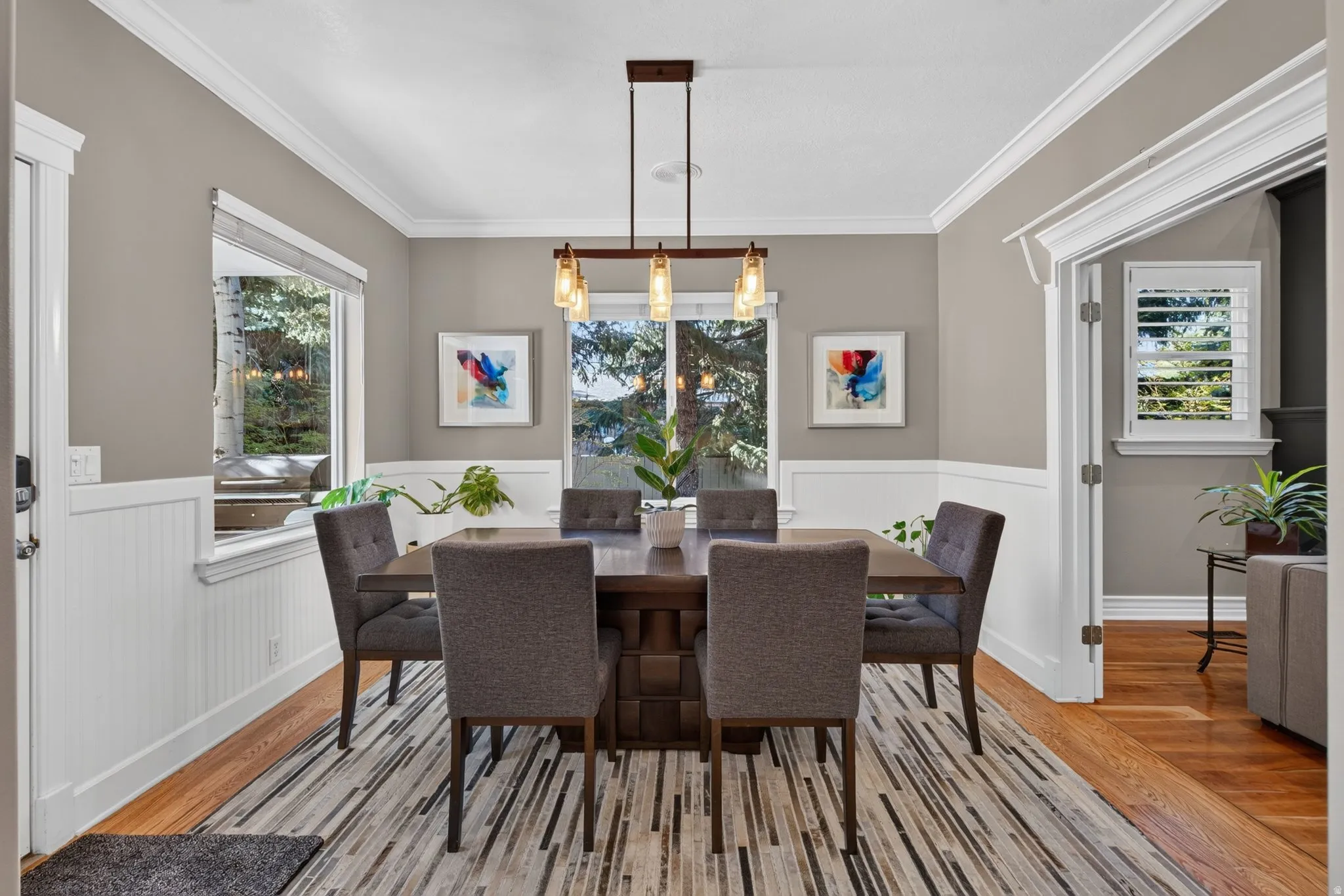 Wood-finish flooring, white wainscoting, crown molding, and a modern linear chandelier