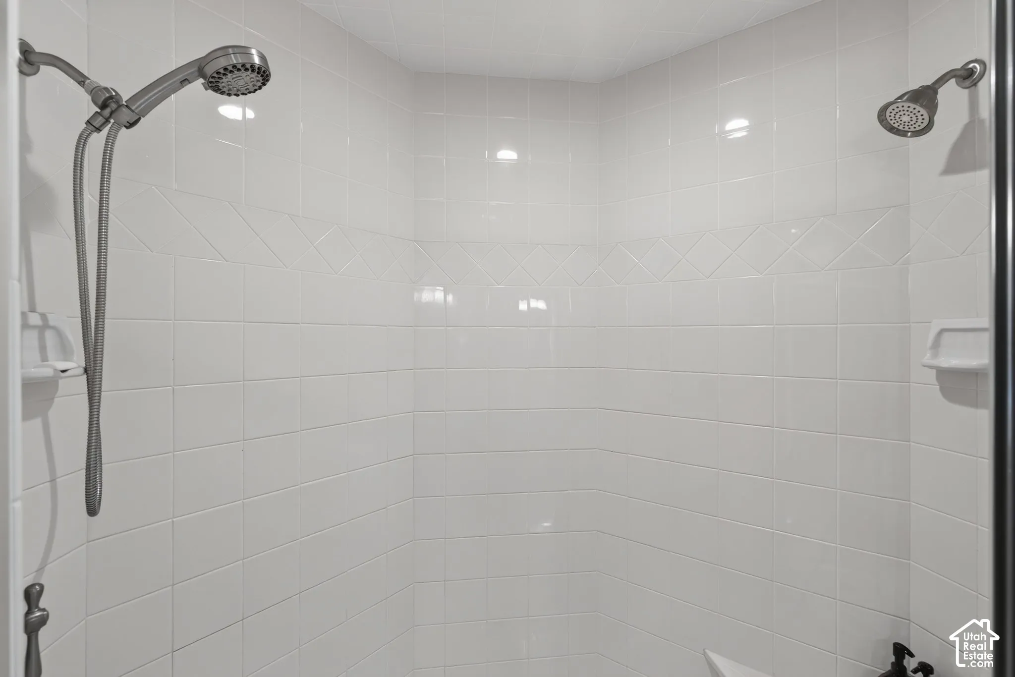 Shower enclosure featuring white ceramic tile walls, decorative accent tile band, fixed shower head, and an additional handheld shower fixture