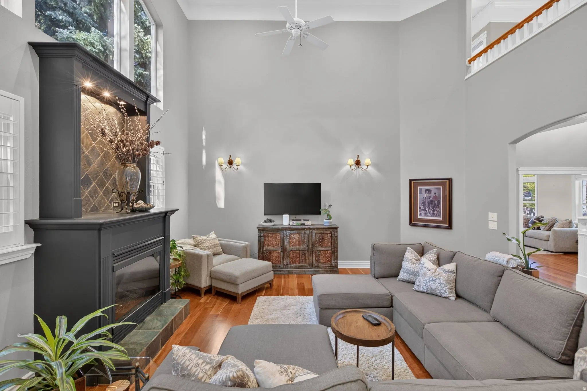 Soaring ceilings featuring a ceiling fan, a fireplace with a tile surround and wood mantel, wood-finish flooring, and a second-story open railing