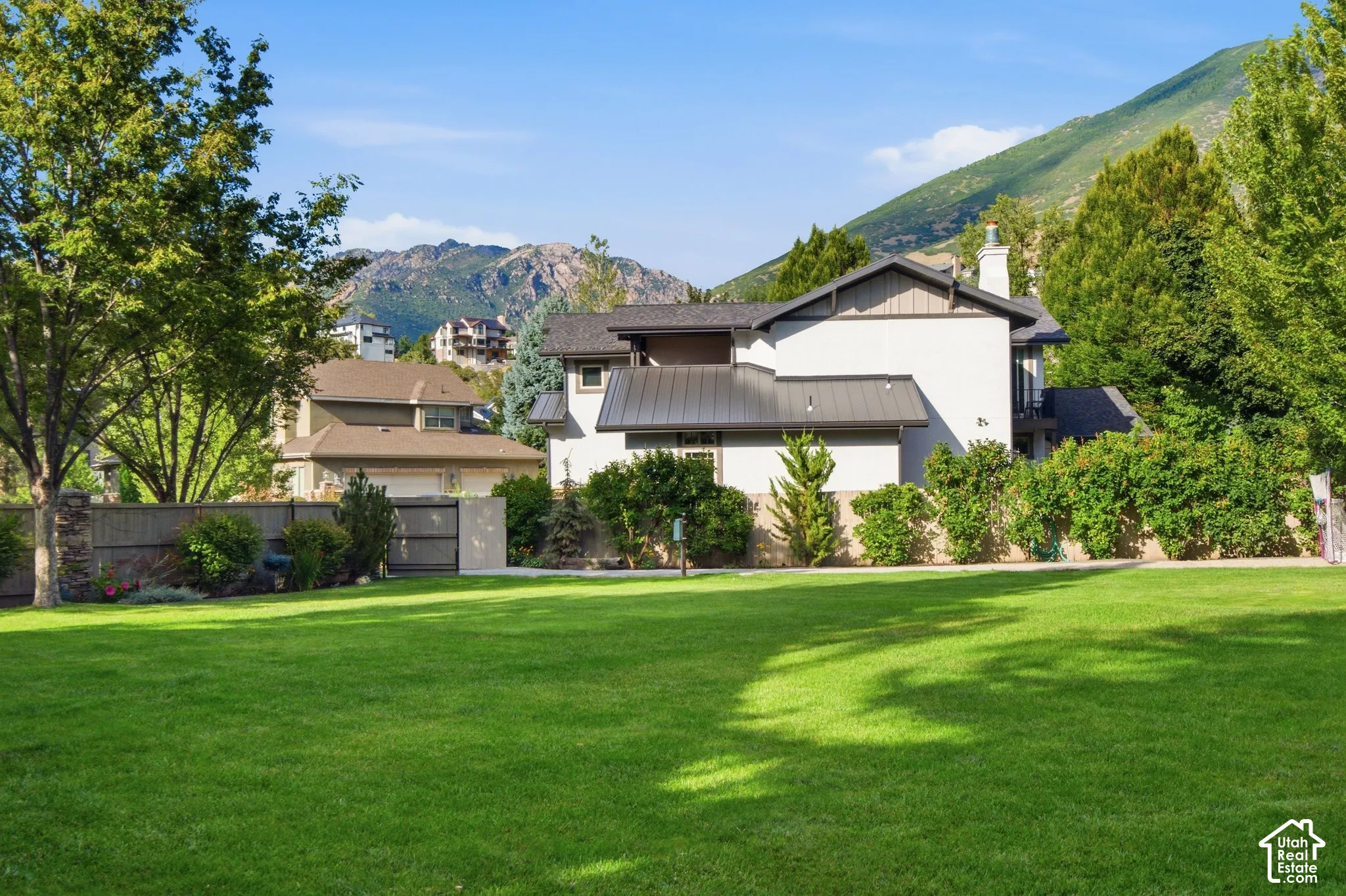 Expansive green lawn, mature trees, mountain backdrop, and stucco exterior with a metal roof