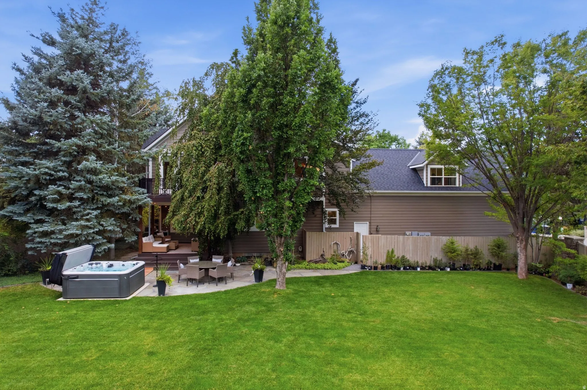 Expansive yard featuring a manicured lawn, a large patio with built-in hot tub, and mature trees