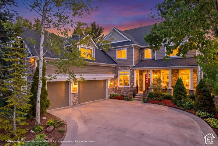 Stone and siding exterior with a covered front porch, integrated two-car garage, and a curved concrete driveway