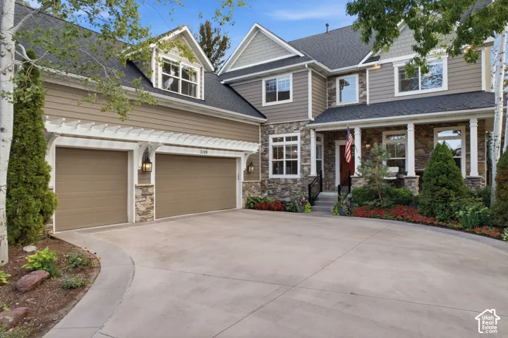 Two-story residence featuring a stone and siding exterior, multi-pane windows, covered entry with pillars, and an attached two-car garage with pergola accents
