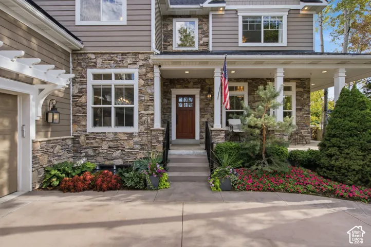 Stone facade with siding accents, covered front porch, white pergola, concrete driveway, and mature landscaping