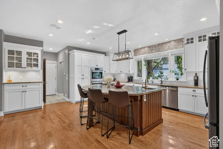Spacious kitchen featuring an island with beadboard paneling, white cabinetry, integrated stainless steel appliances, wood-finish flooring, and a decorative tile backsplash