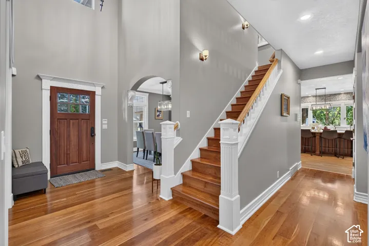 Hardwood flooring throughout the entry, a wood-paneled door with glass inserts, a two-story foyer with sconce lighting, an arched doorway, and a wood staircase with white balusters