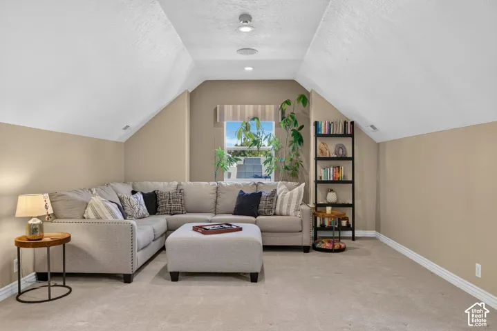 Recessed lighting illuminates a spacious room featuring sloped ceilings and neutral-toned carpeting