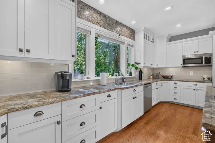 Updated kitchen featuring white cabinetry, stone countertops, stainless steel appliances, a tile backsplash, and wood-finish flooring