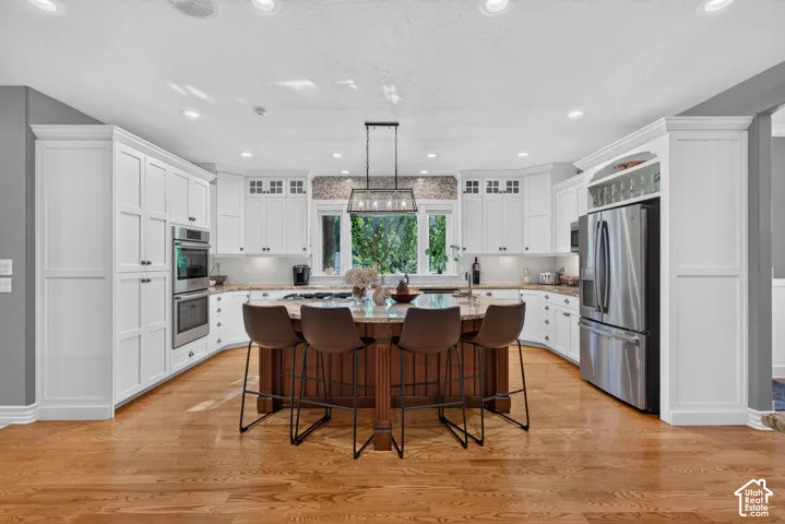 Spacious kitchen featuring white cabinetry, a large central island with seating, stainless steel appliances, wood-finish flooring, and recessed lighting