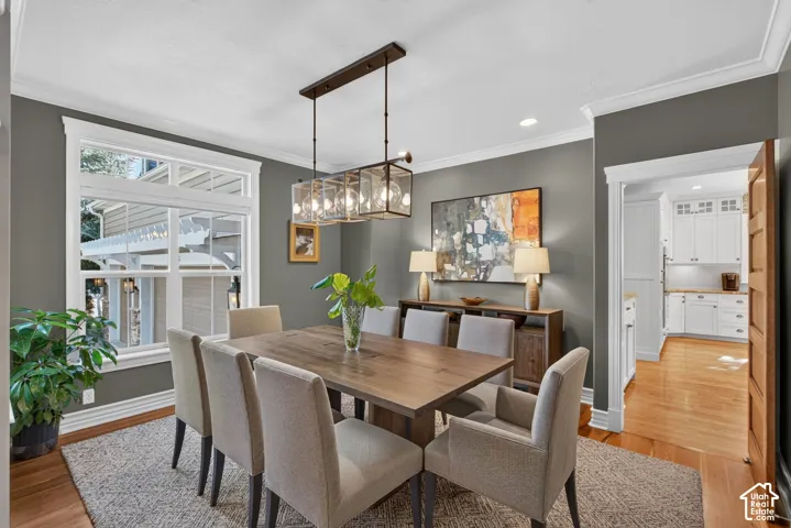 Dining area featuring wood-finish flooring, a large window with transom, crown molding, and a multi-light linear chandelier