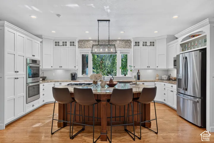 White shaker cabinetry, stainless steel double ovens, wood-finish flooring, central island with seating, and a mosaic tile backsplash